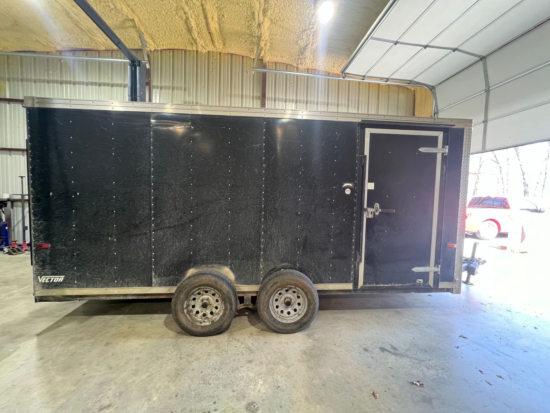 Black enclosed trailer with two axles parked inside a large garage or warehouse.