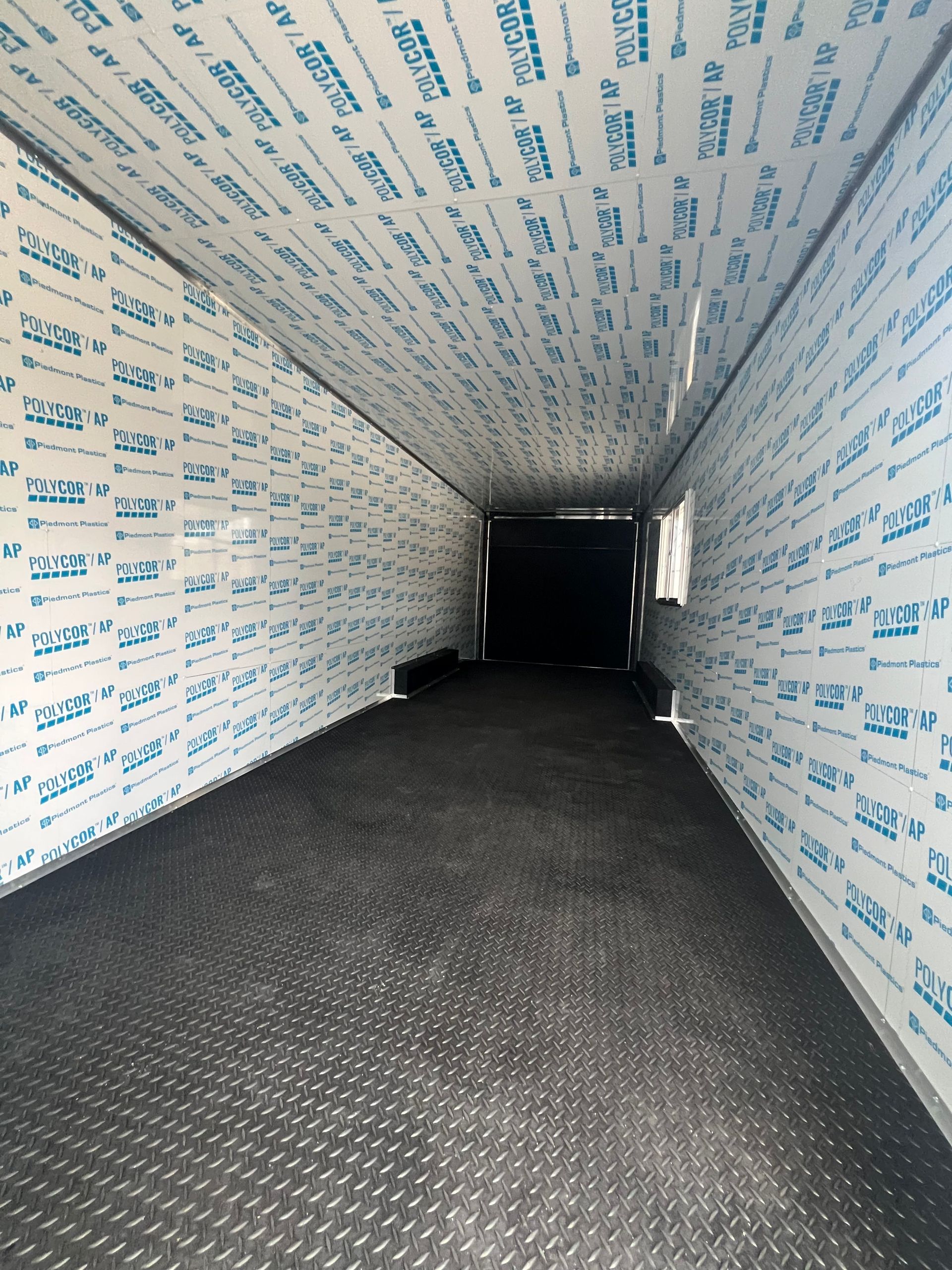 Empty modern cargo trailer interior lined with white insulation, leading to a dark opening over a black floor covering
