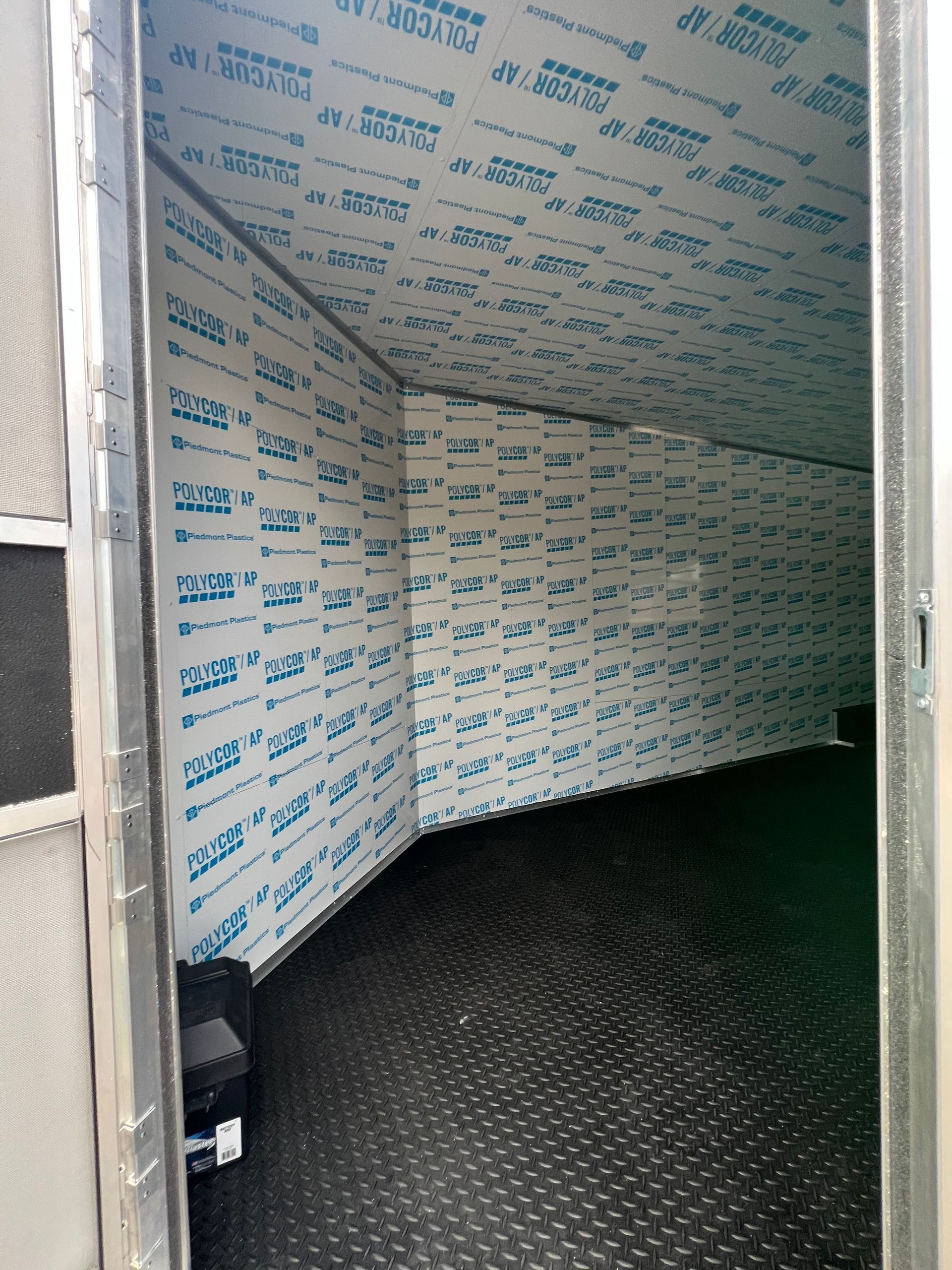 Insulated enclosed trailer interior with white walls, blue text, and black diamond-plate floor