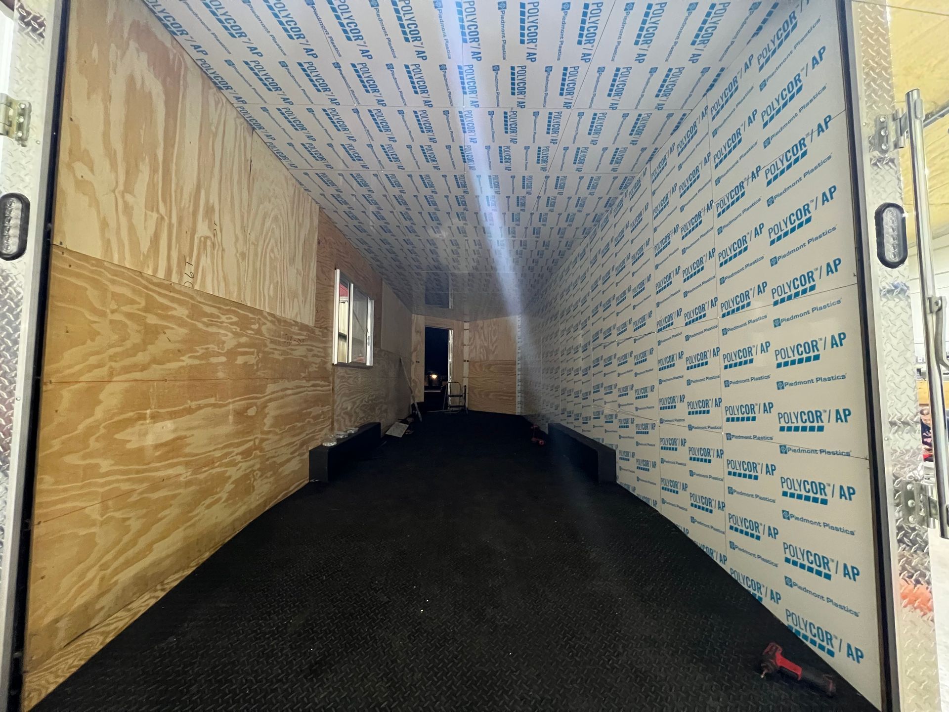 Plywood interior of a cargo trailer under upgrade construction with rubber floor, and insulated ceiling and right wall