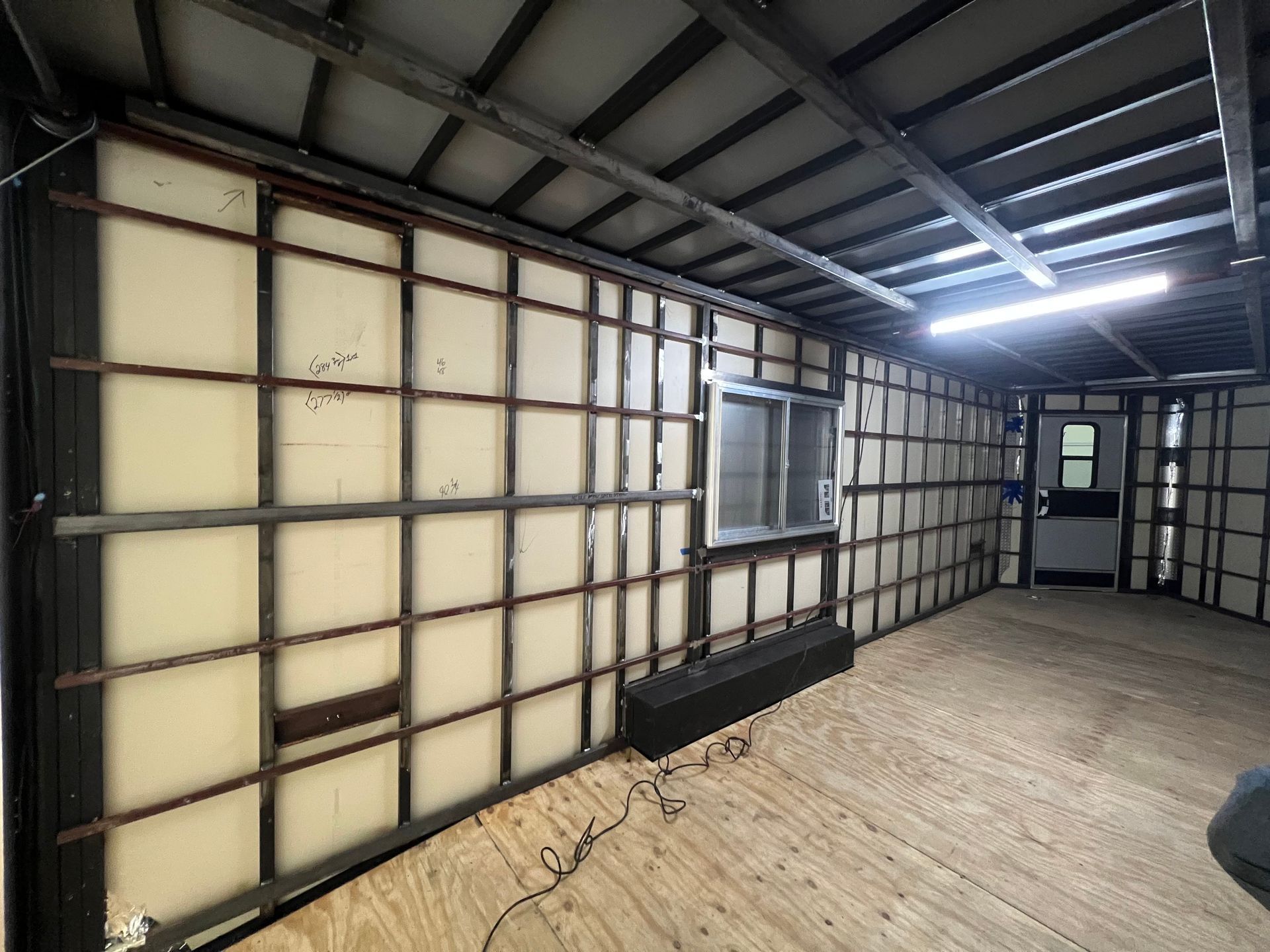 Bare interior of a partially renovated cargo trailer with exposed framing, insulation, and a concrete floor.