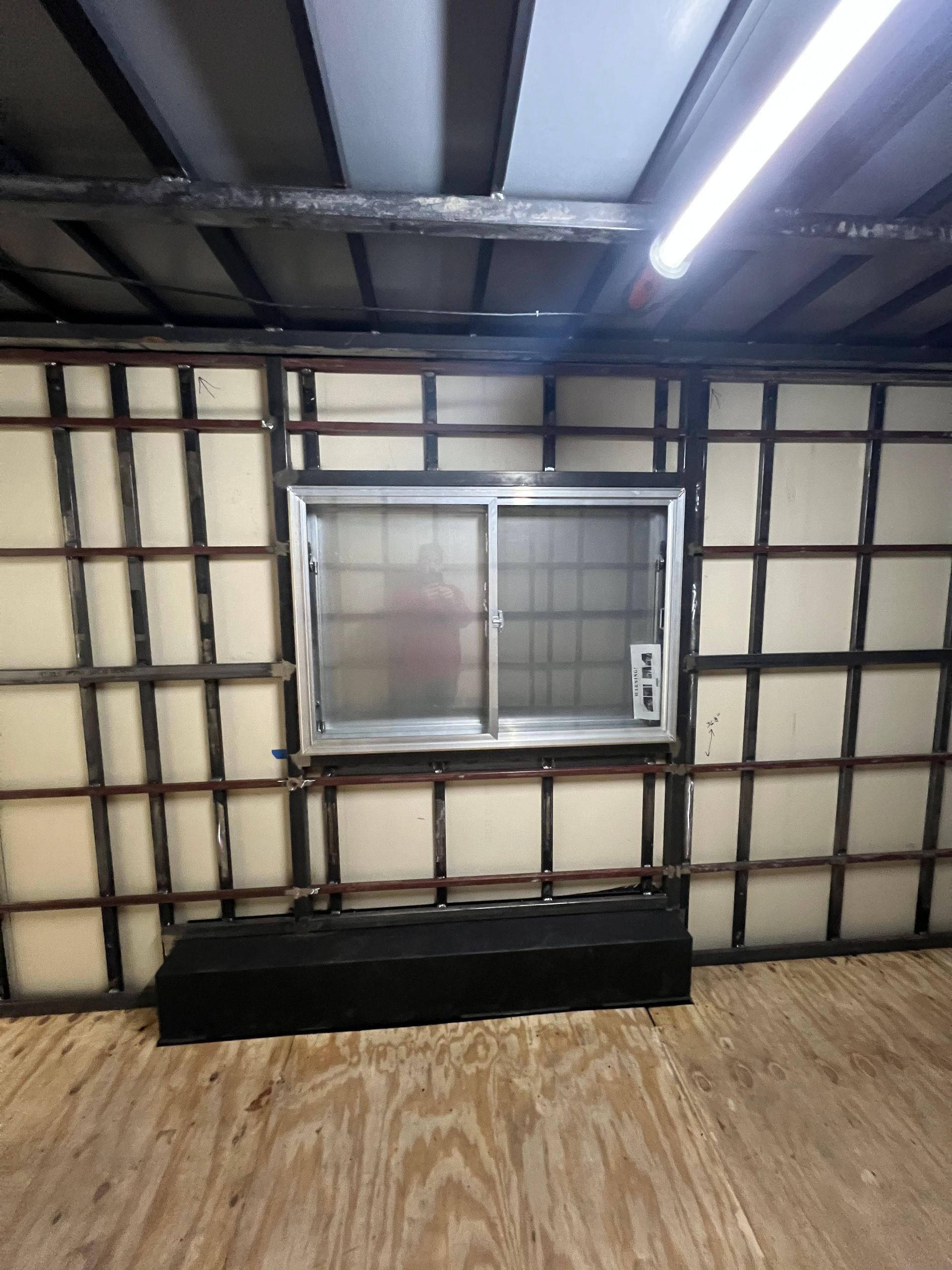 Interior of a long cargo truck trailer with a wall-mounted window air conditioner, wood floor, and exposed ceiling beams.