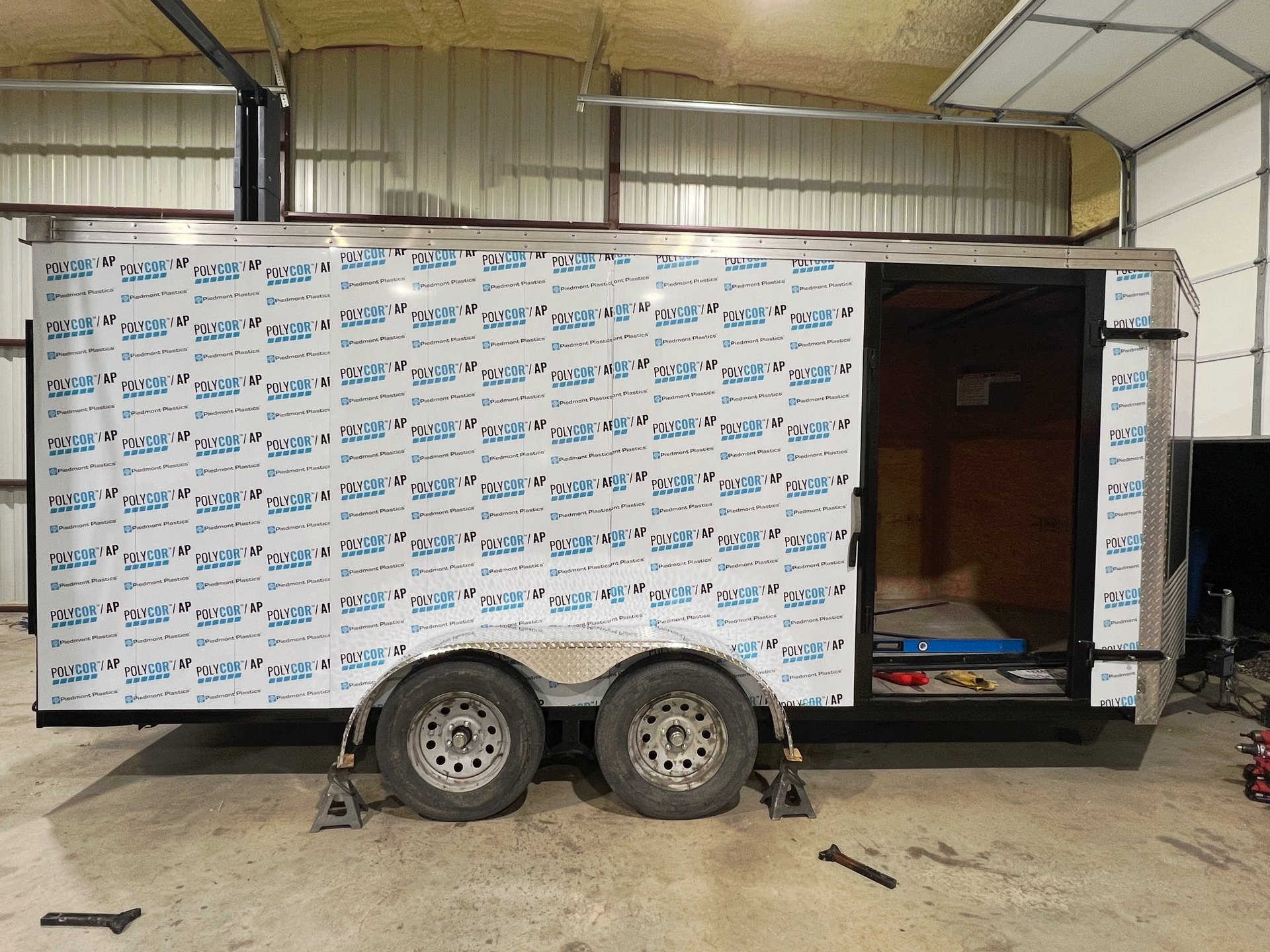 White enclosed trailer with side door open inside a warehouse, showing a partially built interior.