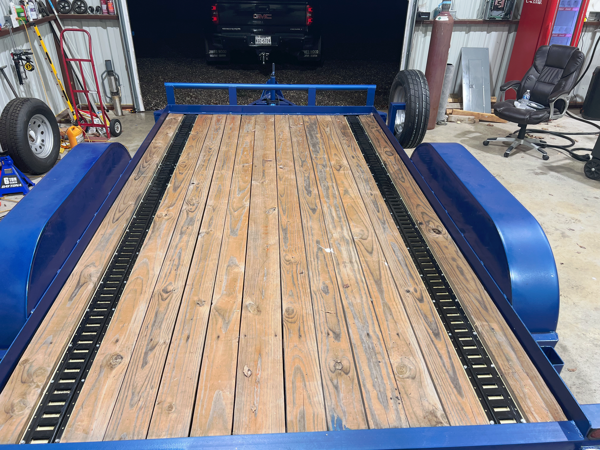 Custom built wooden car trailer deck with blue fenders inside an auto repair shop