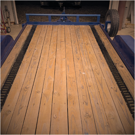 Wooden trailer bed with blue side rails and large tires, viewed from the rear.