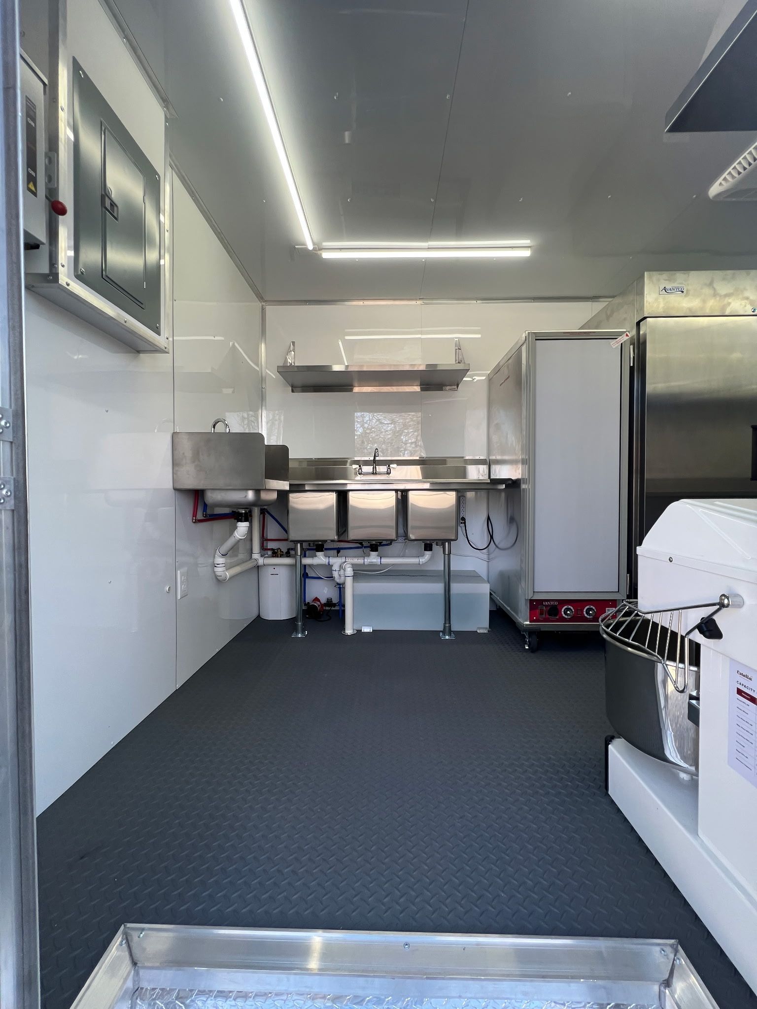 Empty mobile kitchen interior with stainless steel counters, white walls, and dark carpeted floor