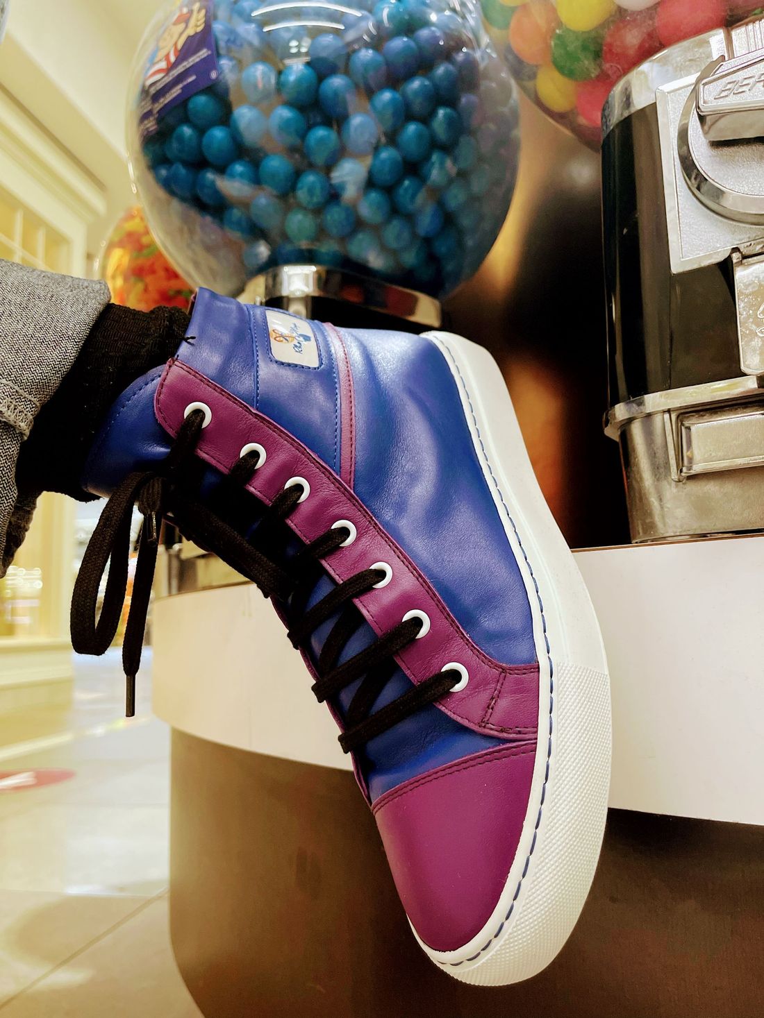A person wearing a pair of purple and blue sneakers next to a gumball machine