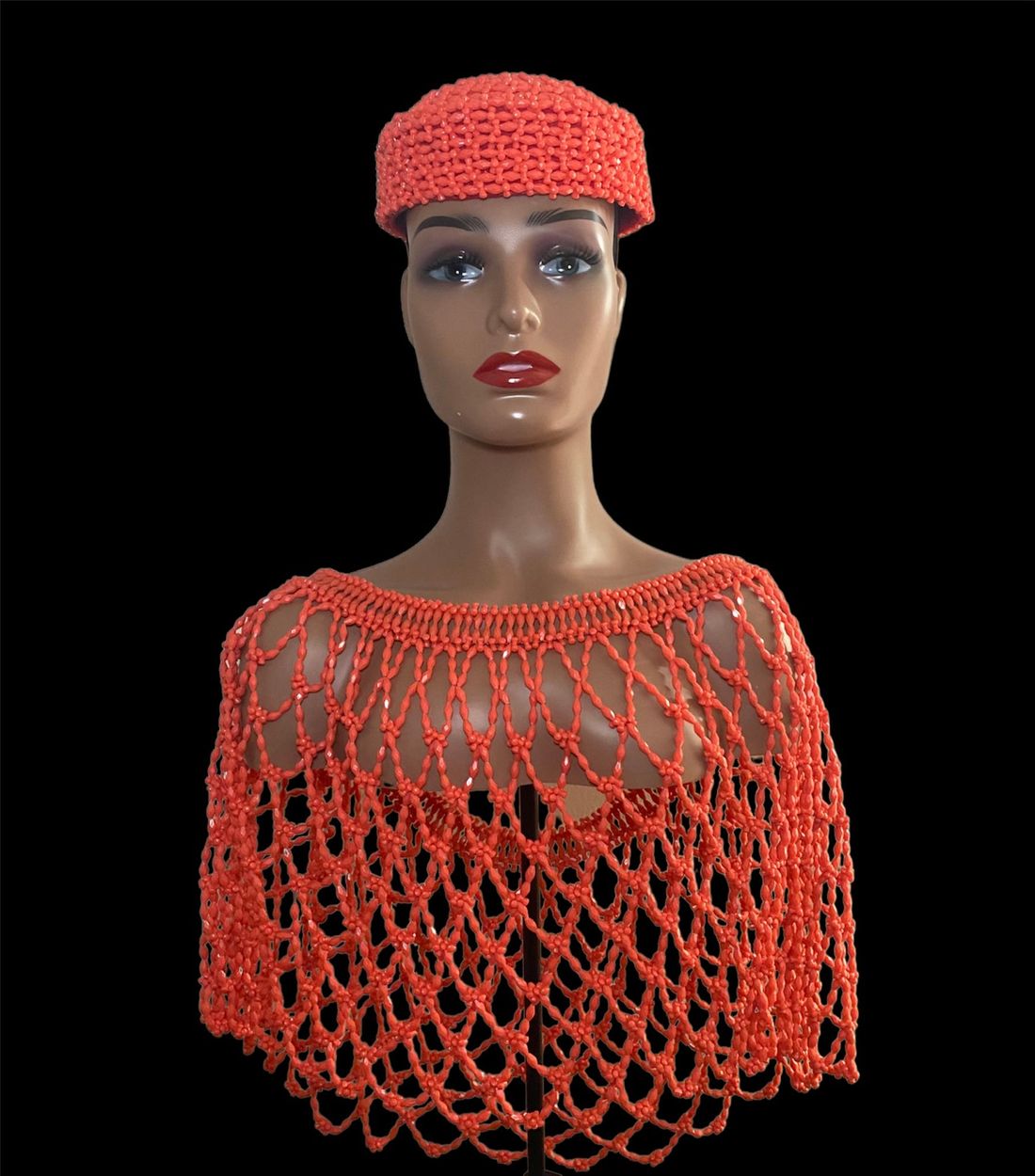 A mannequin is wearing an orange hat and a red cape.