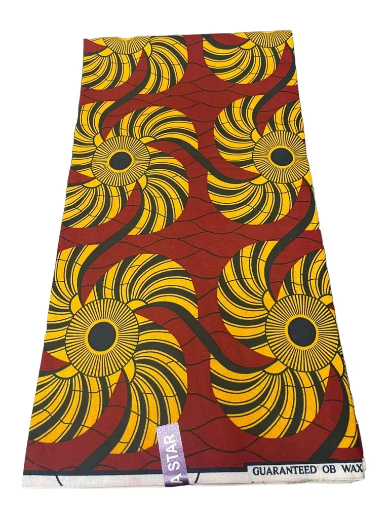 Bright red and yellow patterned wax print fabric with circular swirl motifs, folded flat.