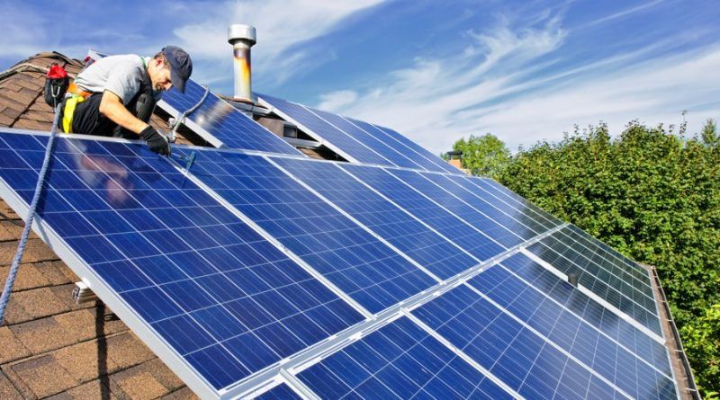 Worker cleaning blue solar panels on a rooftop under a bright sky