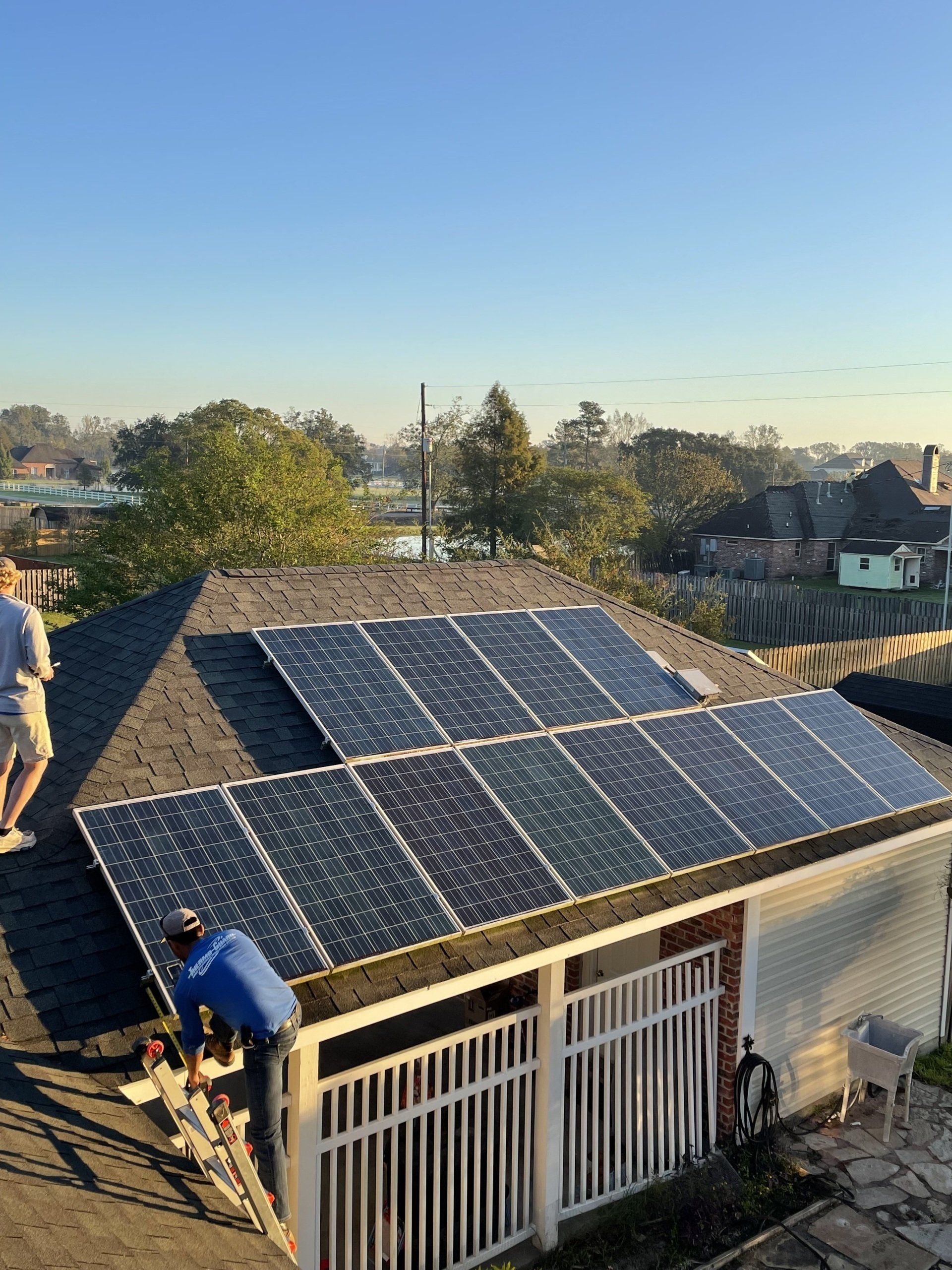 Roof with solar panels; two workers install them on a house at sunset.