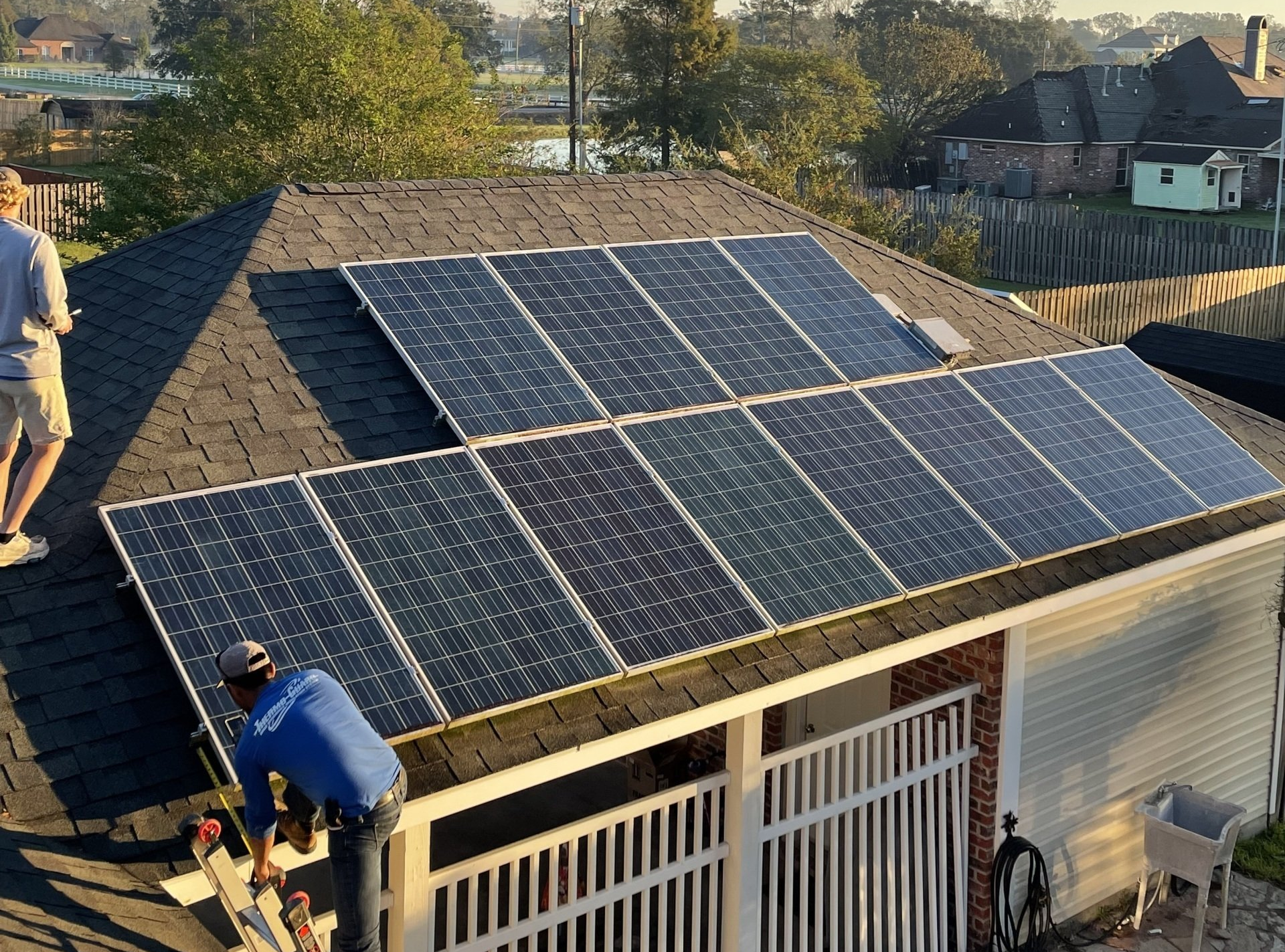 Roof with solar panels; two workers install them on a house at sunset.