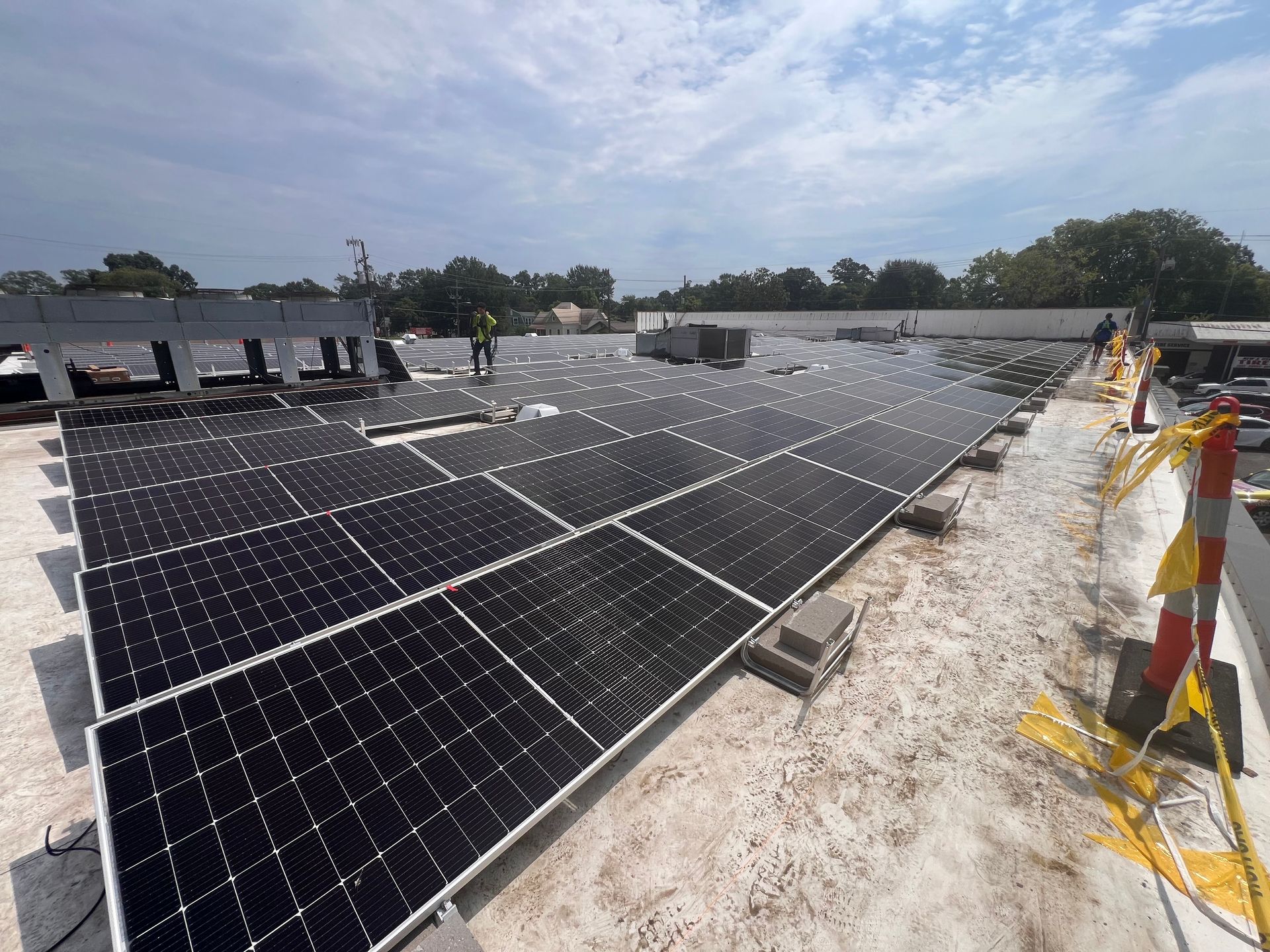 Solar panels installed on a rooftop under a bright sky, with workers visible in the distance.