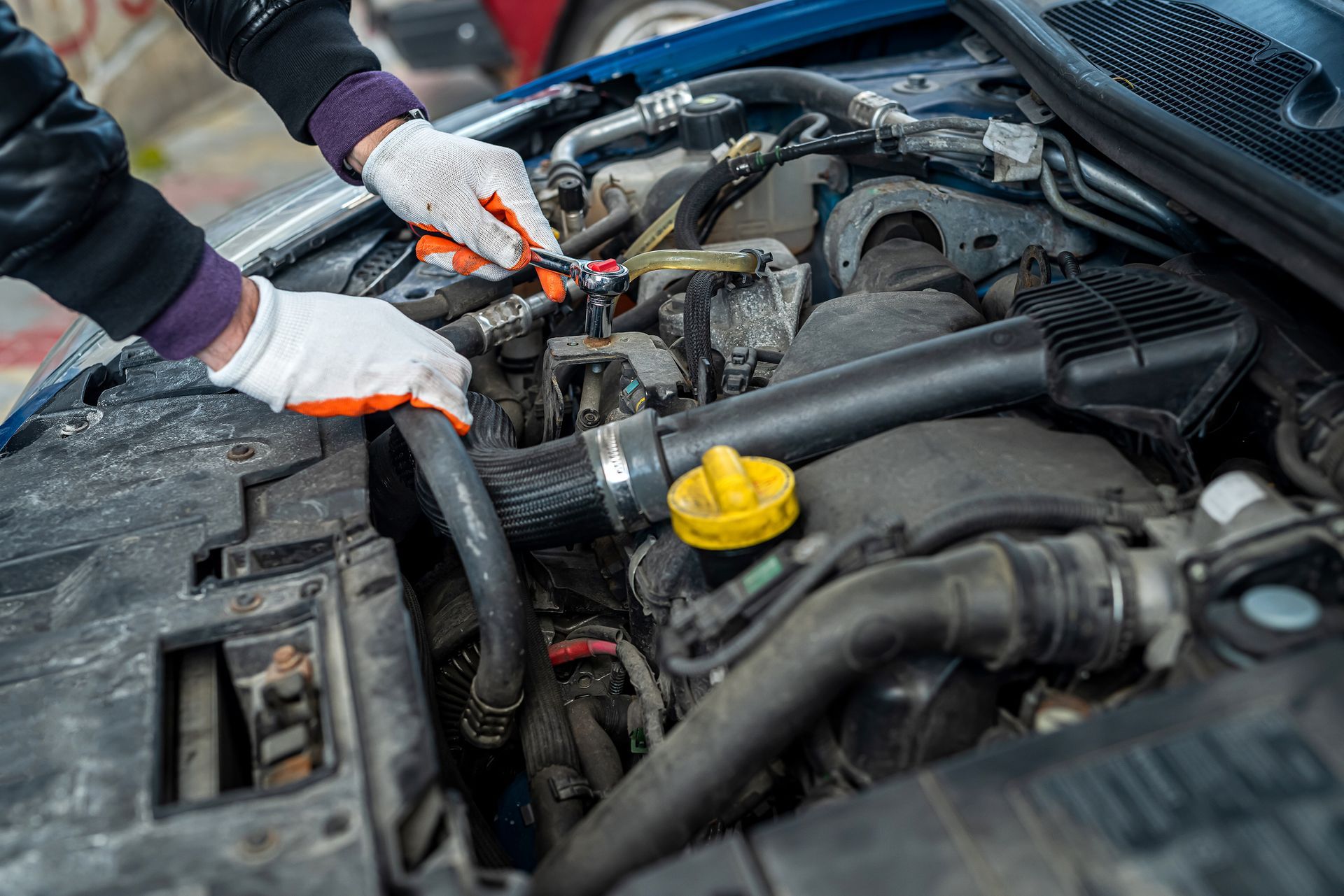 Hands in work gloves working on a car engine, tools in hand, blue car hood.