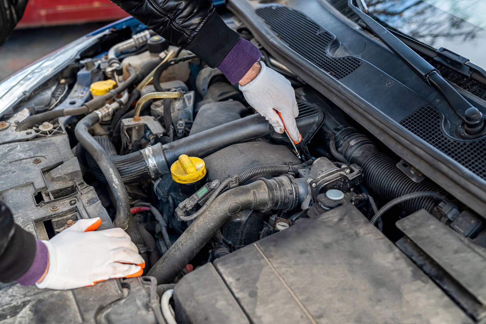 Person wearing gloves examining a car engine.
