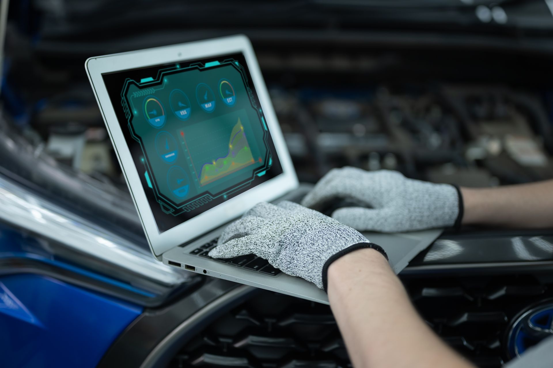 Person in gloves using laptop to diagnose a car engine; blue vehicle, indoor setting.