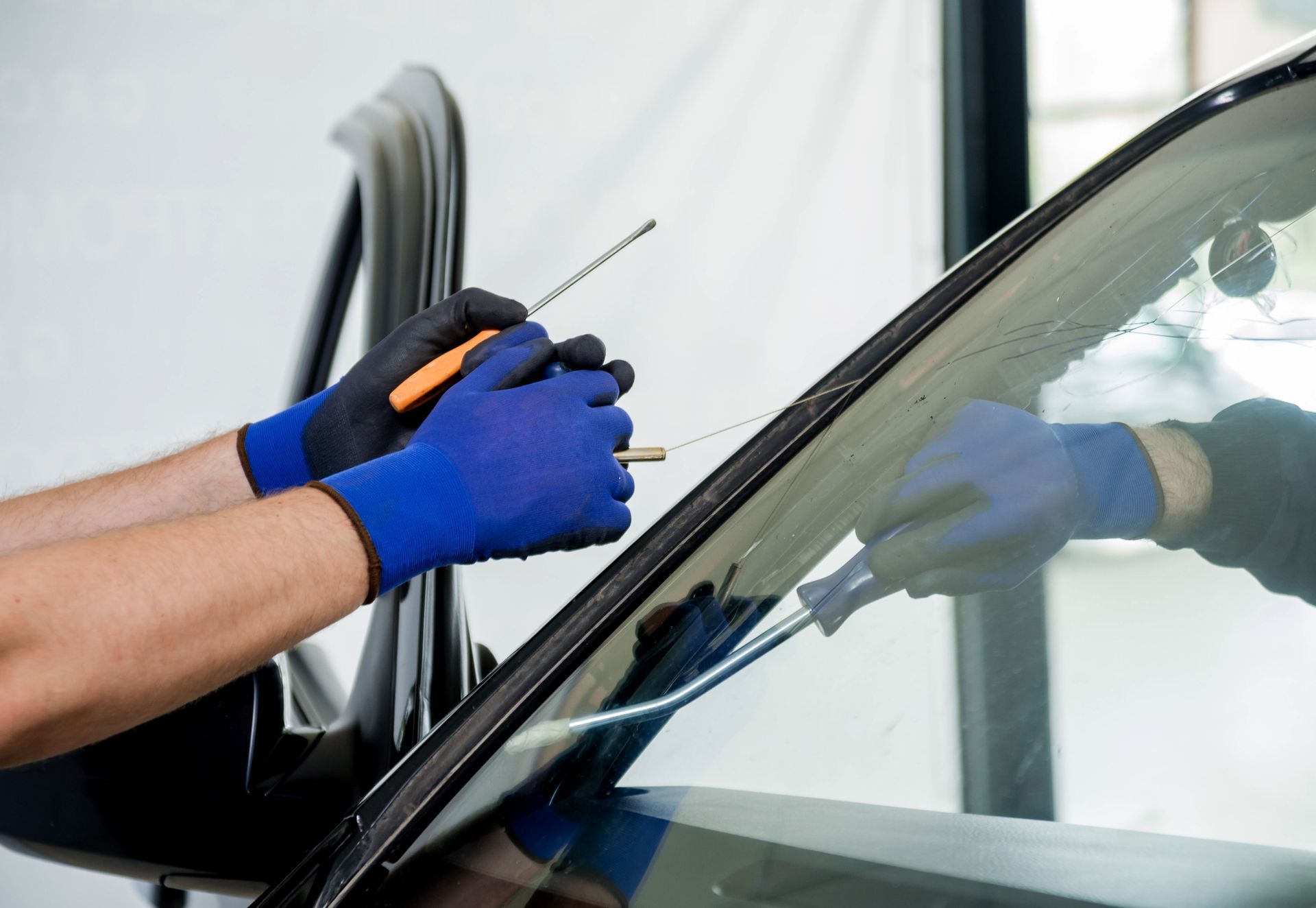 Hands in blue gloves working on car windshield.
