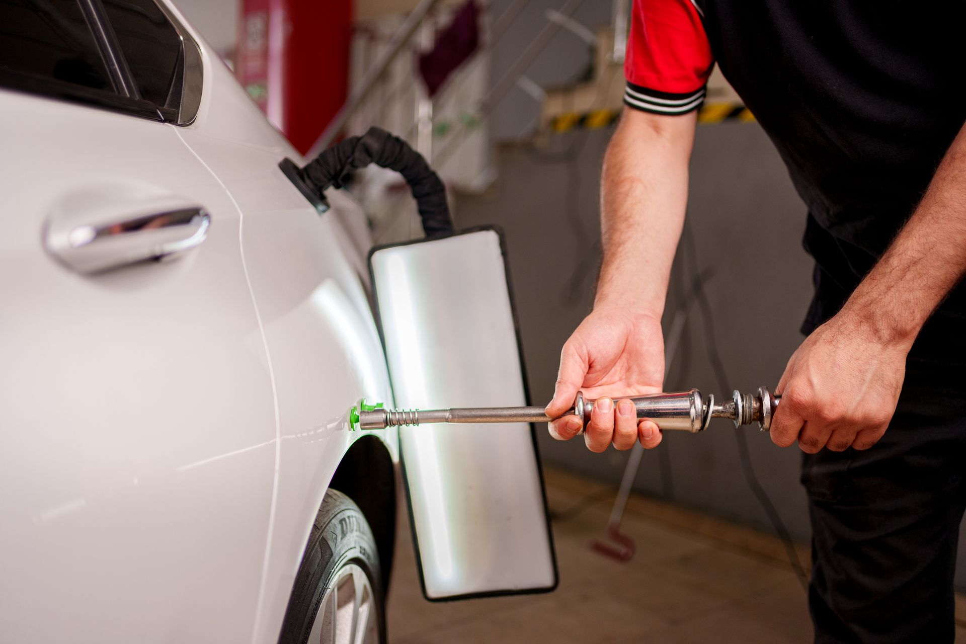 Mechanic using a tool to remove a dent from a white car in a garage.