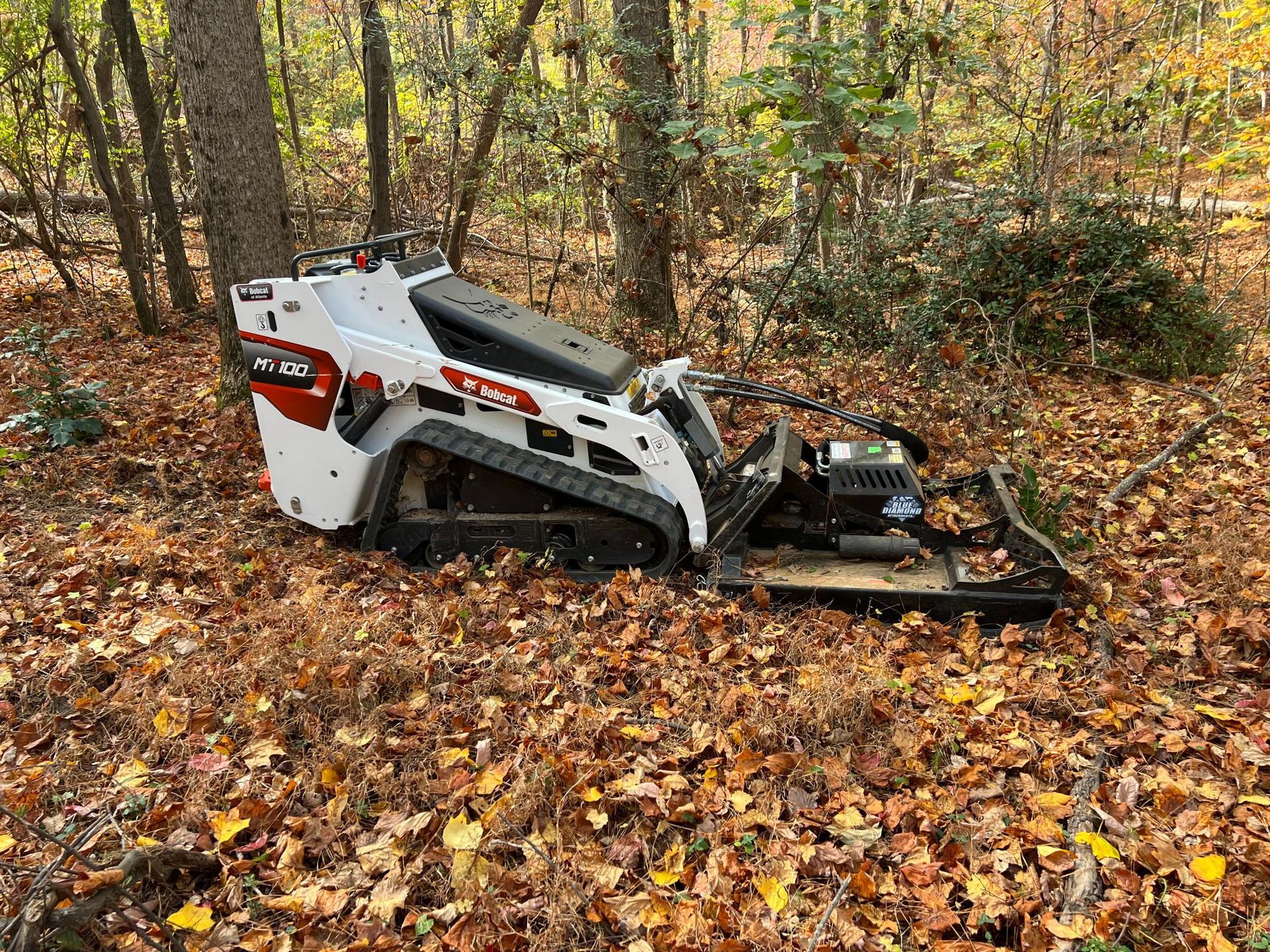 A small tractor is sitting on top of a pile of leaves in the woods.