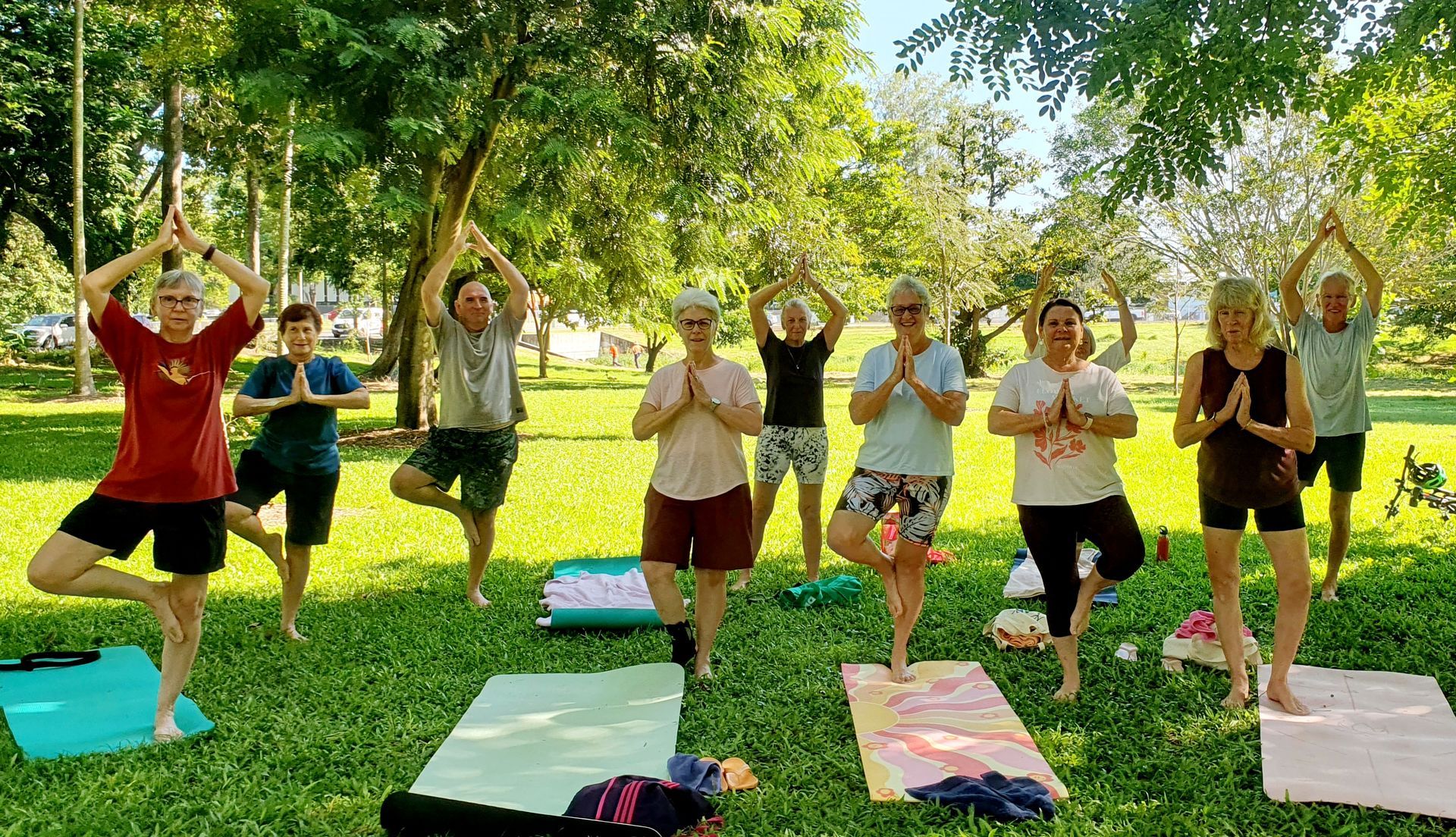 People doing yoga poses on mats in a sunny park under trees