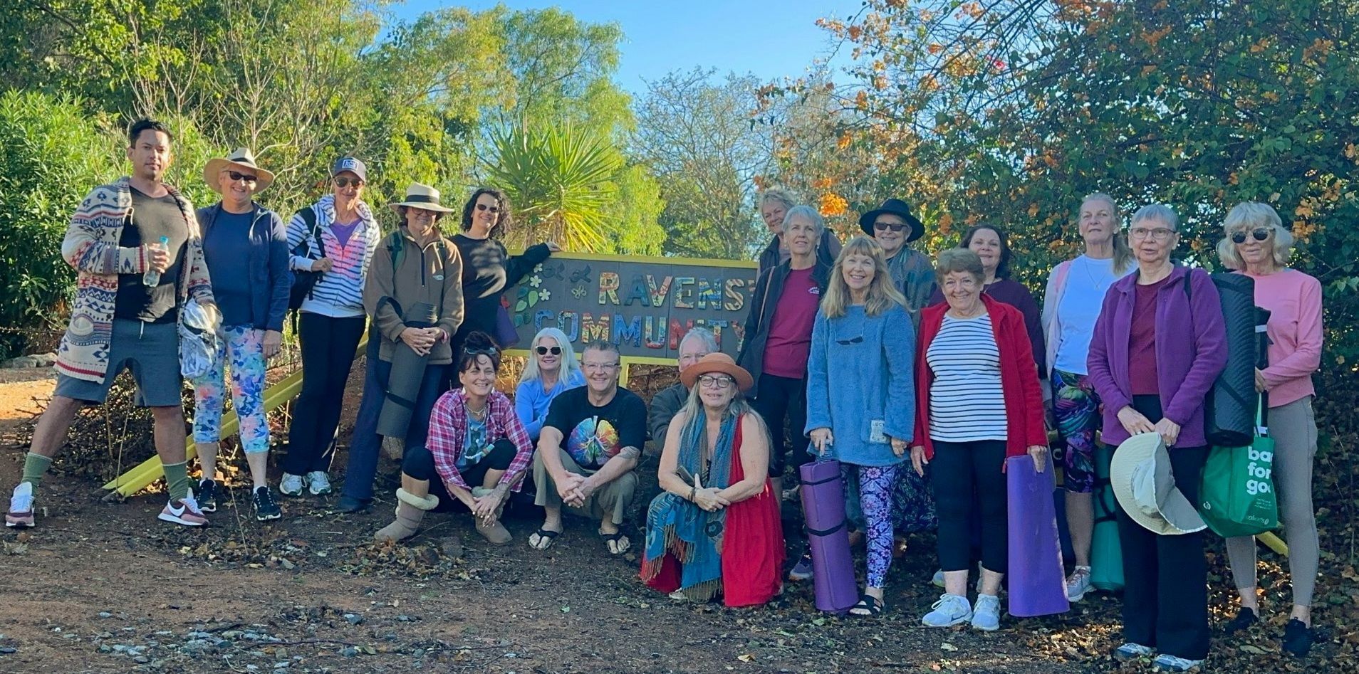 Group of people posing outdoors on a sunny trail beside a bench and trees