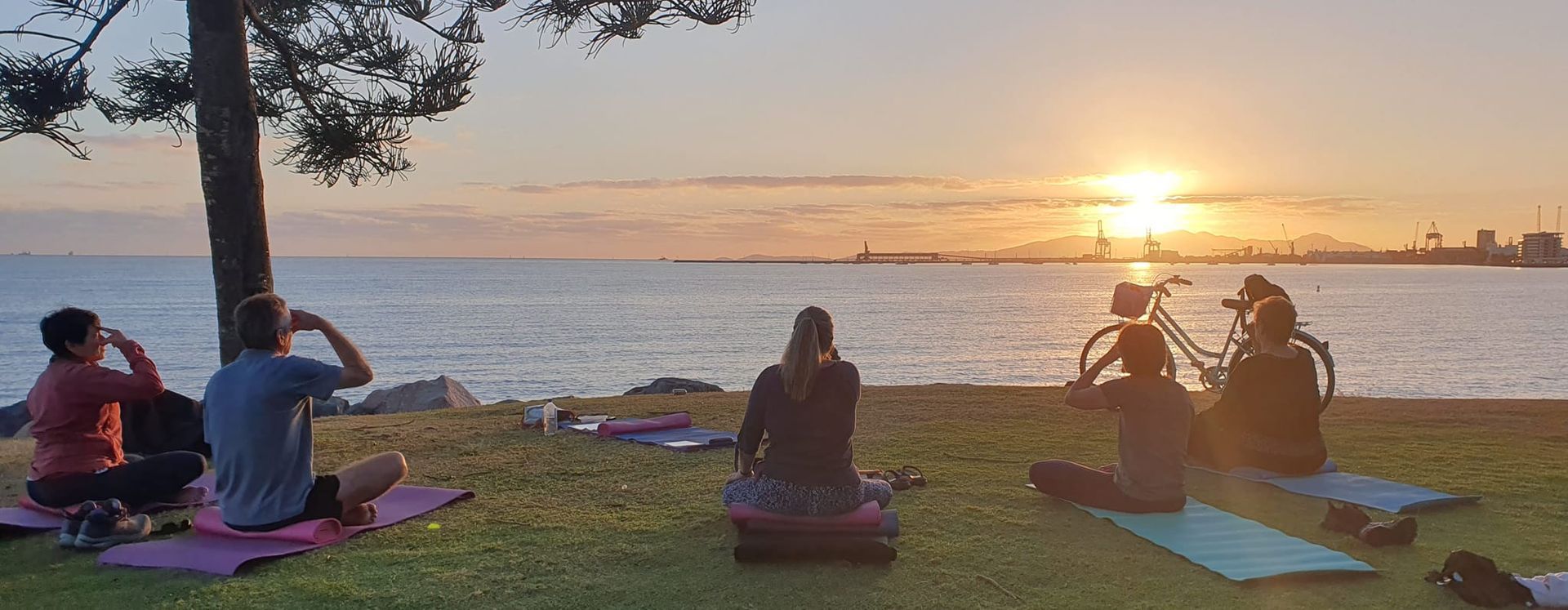People Doing Yoga on Mats Near the Ocean at Sunset With a Bicycle Visible — Skilful Living in North Ward, QLD