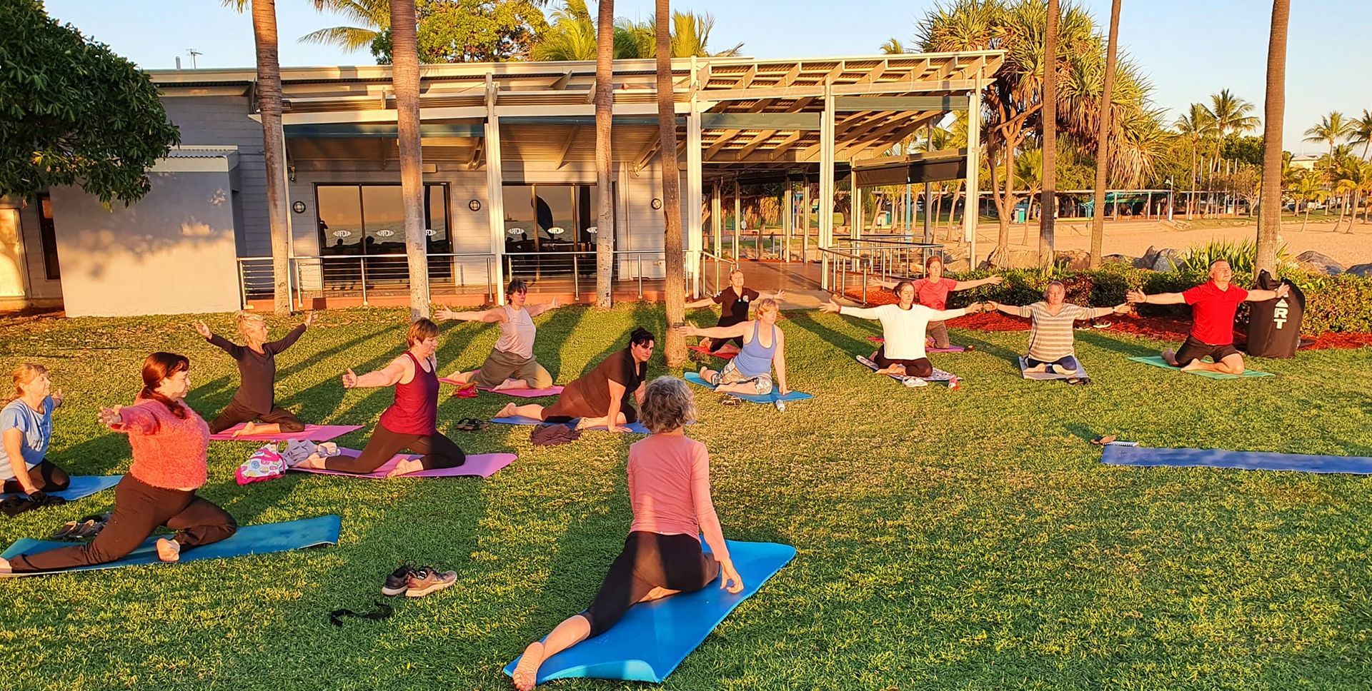A Group Practices Yoga on a Grassy Lawn Near a Building With a Canopy — Skilful Living in North Ward, QLD