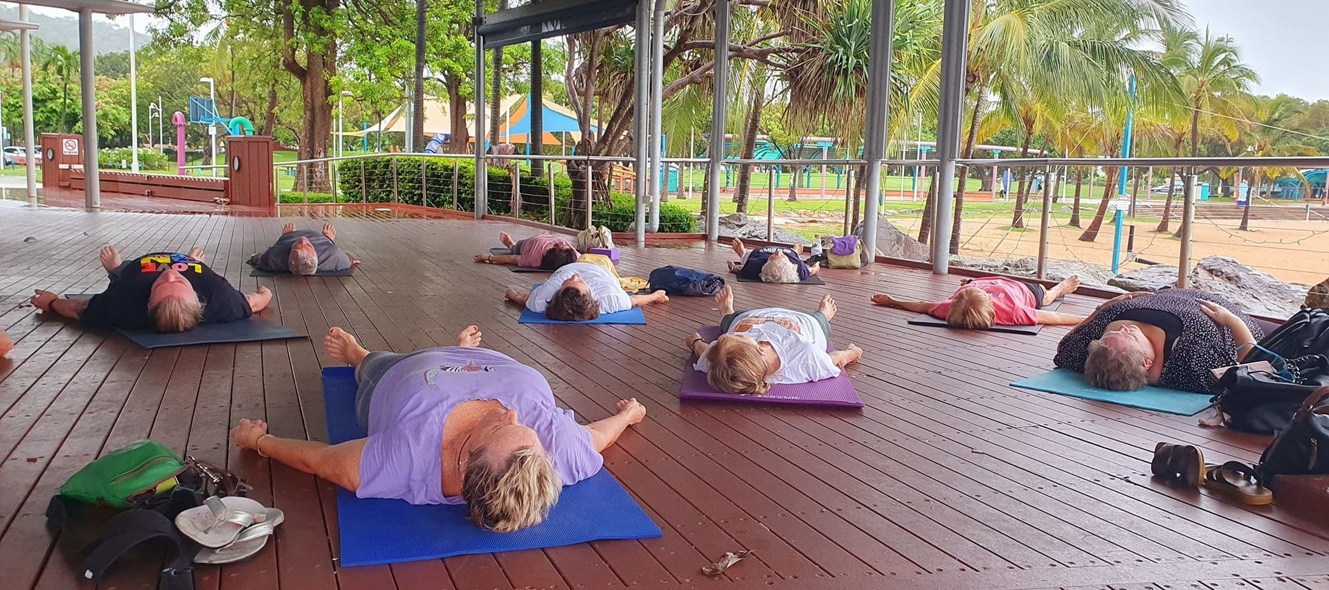 People on Yoga Mats Lying on Their Backs on a Wooden Deck Outdoors — Skilful Living in North Ward, QLD