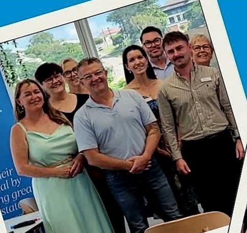 Seven adults smiling for a group photo in front of a bright windowed office setting.