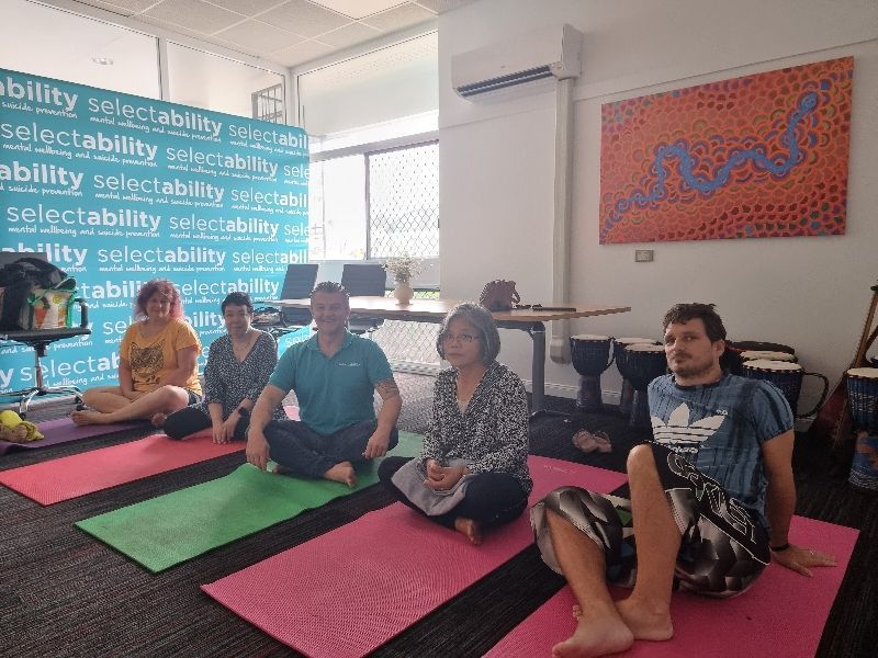 People seated on yoga mats in a bright room, with wall art and a large “selectability” banner.