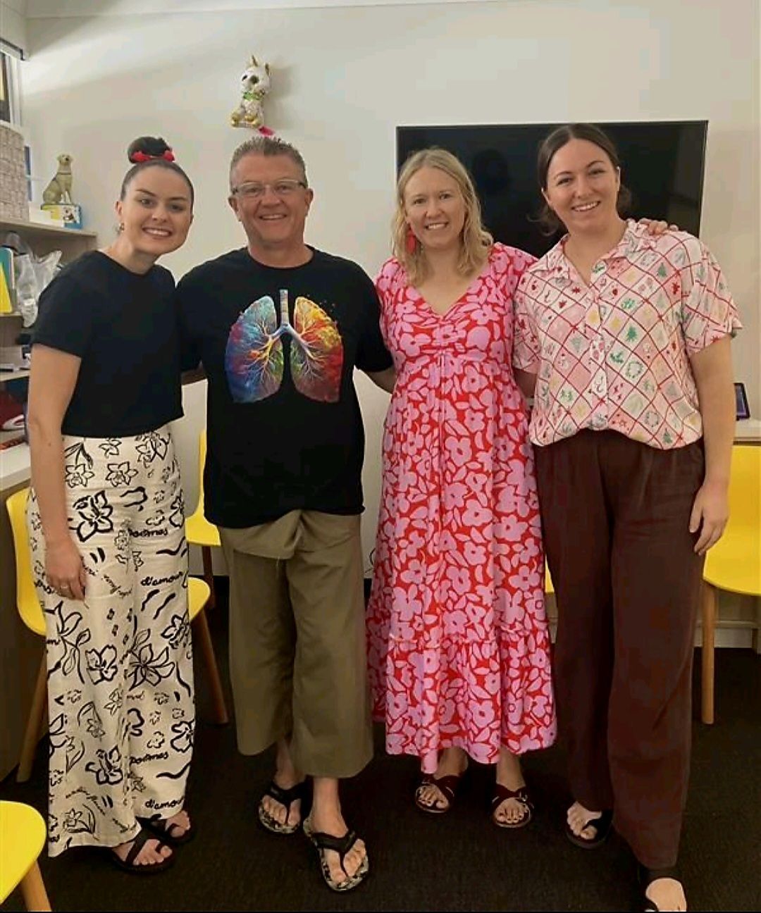 Four people standing together indoors, smiling, wearing colourful outfits.