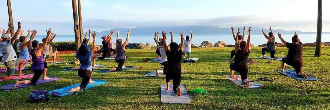 People Practising Yoga on a Grassy Area Near a Body of Water, Raising Their Arms Up — Skilful Living in North Ward, QLD
