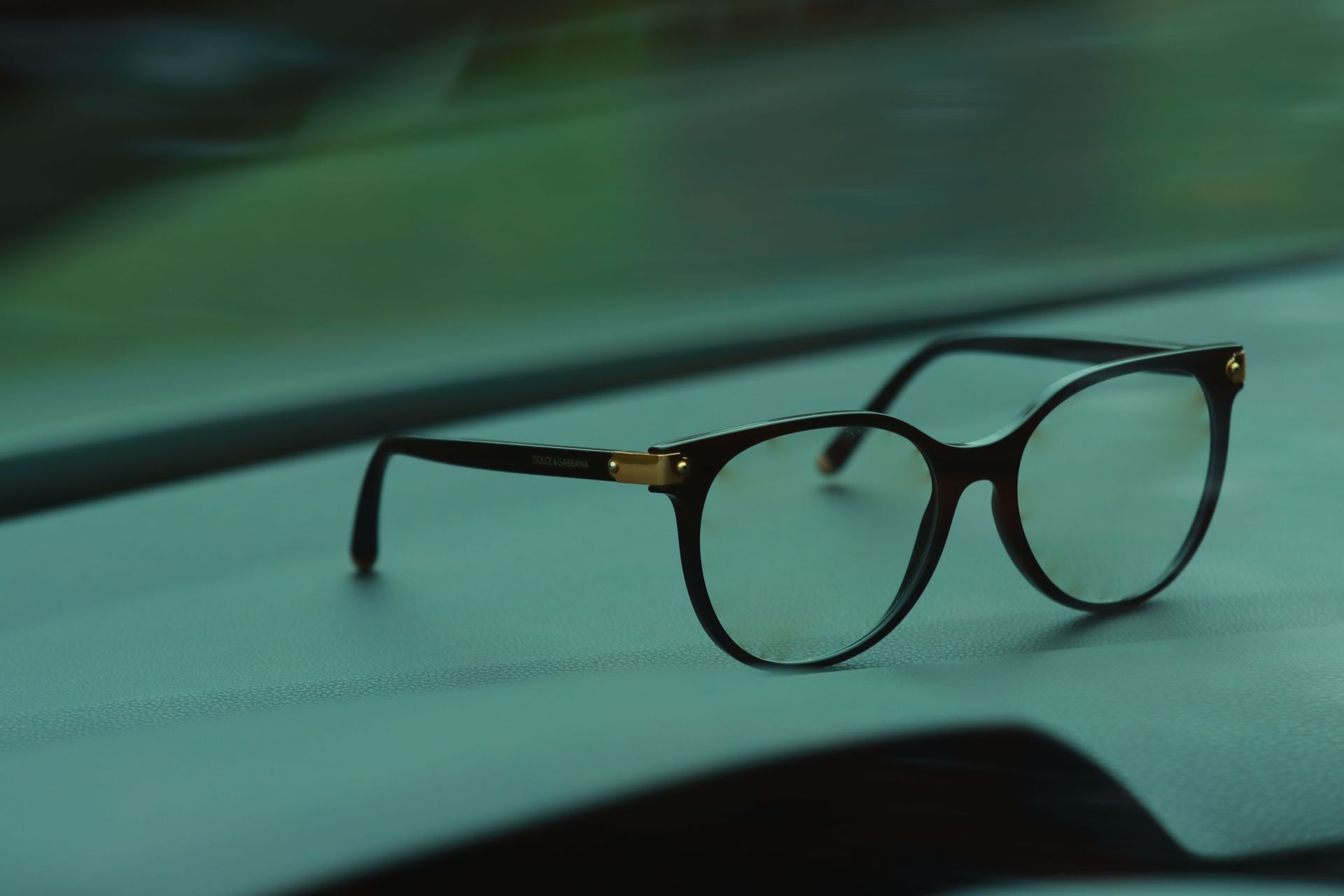Black eyeglasses resting on a teal surface with a blurred green background