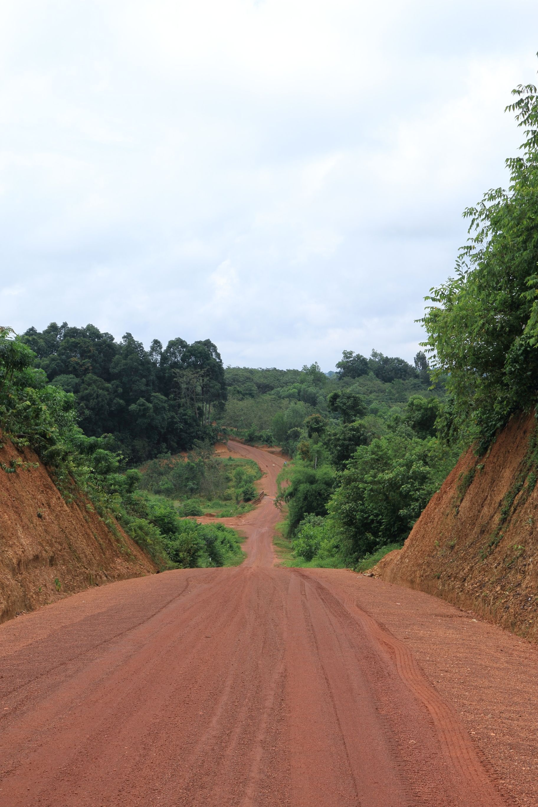 Red dirt road winding through green hills under a cloudy sky