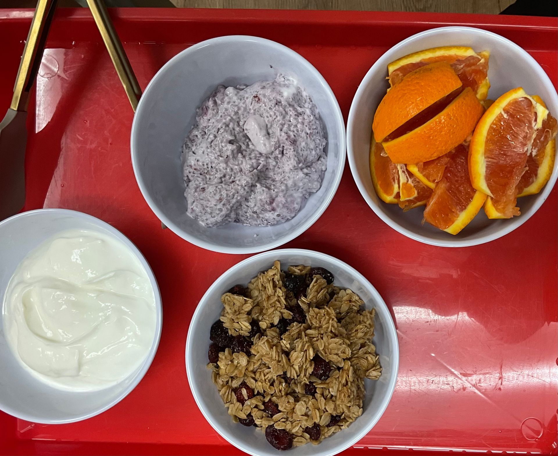 A red tray with bowls of food including granola yogurt and oranges