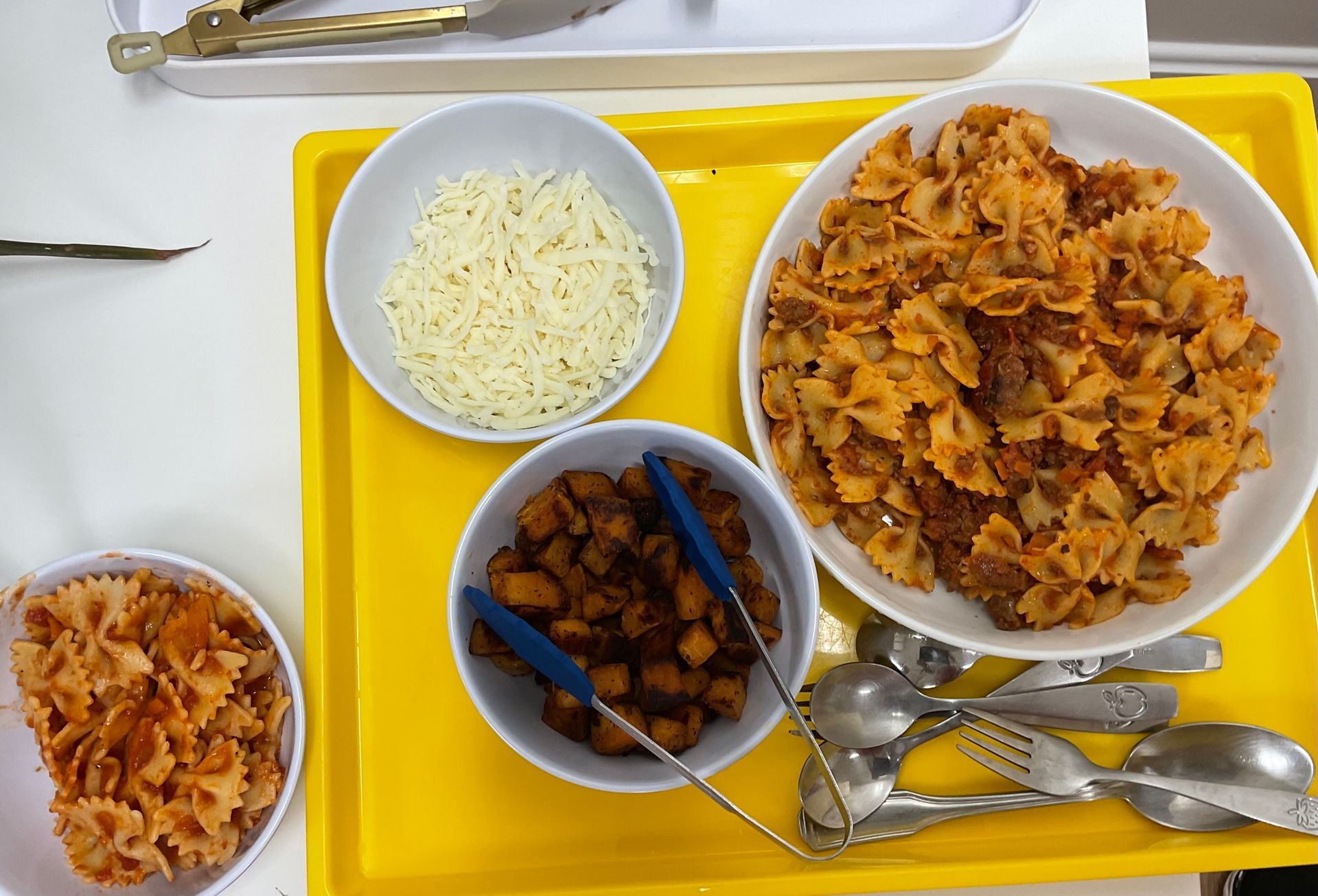 A yellow tray with bowls of food and tongs on it