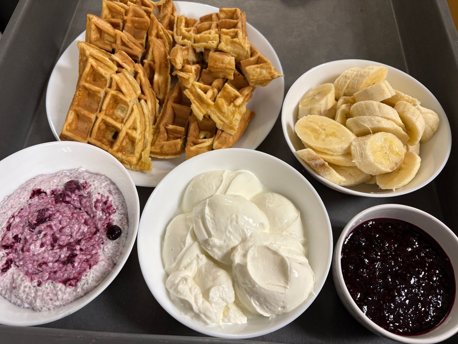A tray of food with waffles, bananas, blueberry sauce and whipped cream