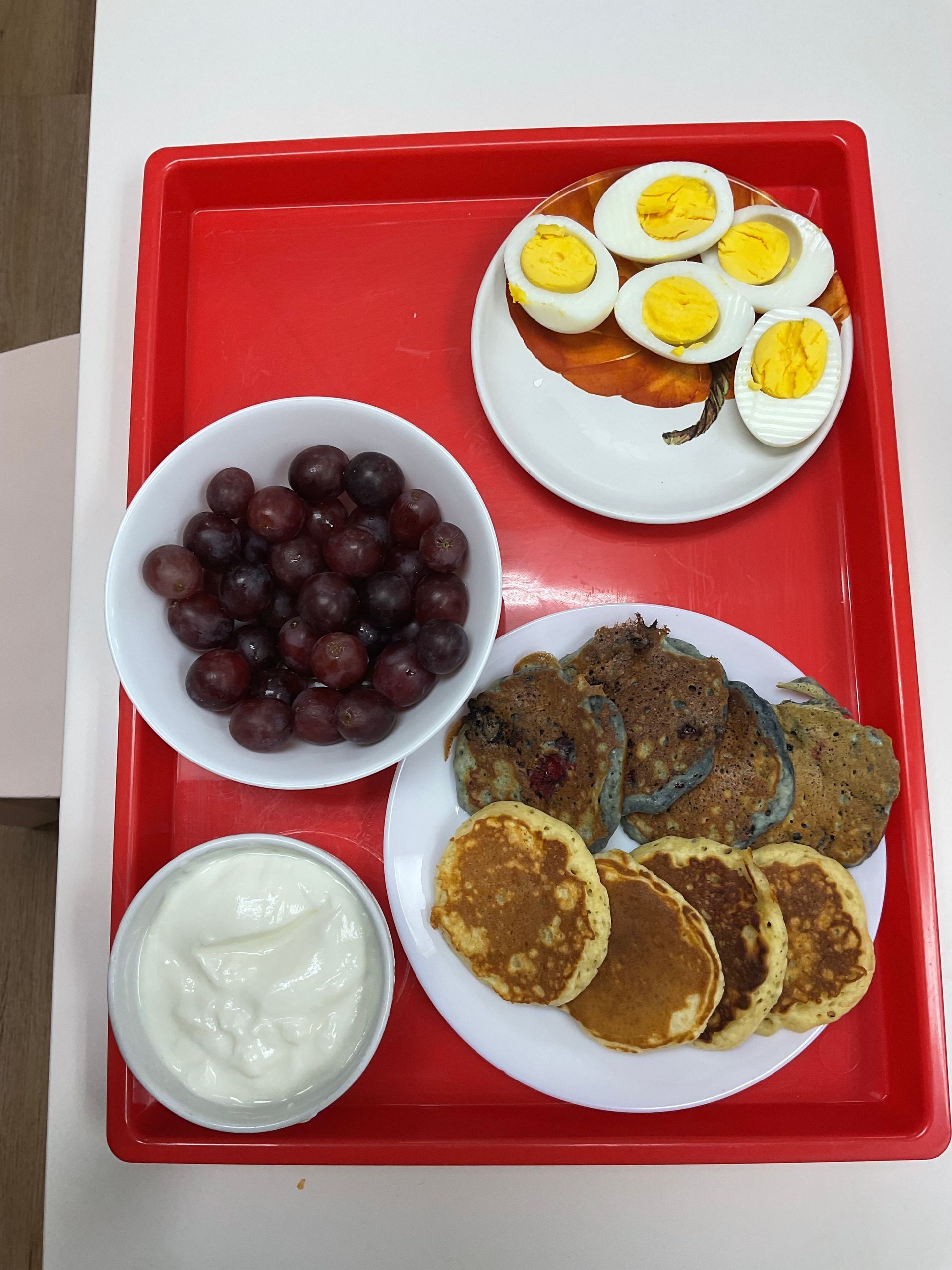 A tray of food including pancakes eggs and grapes