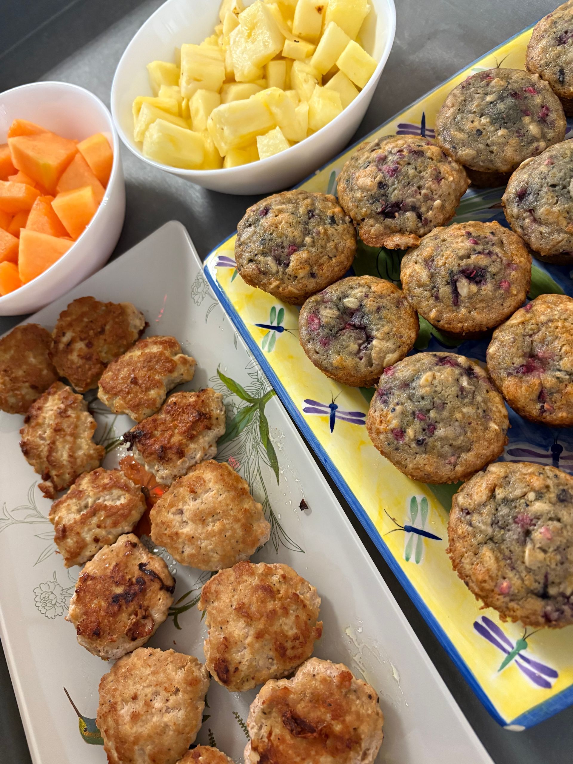 A tray of muffins next to a bowl of fruit