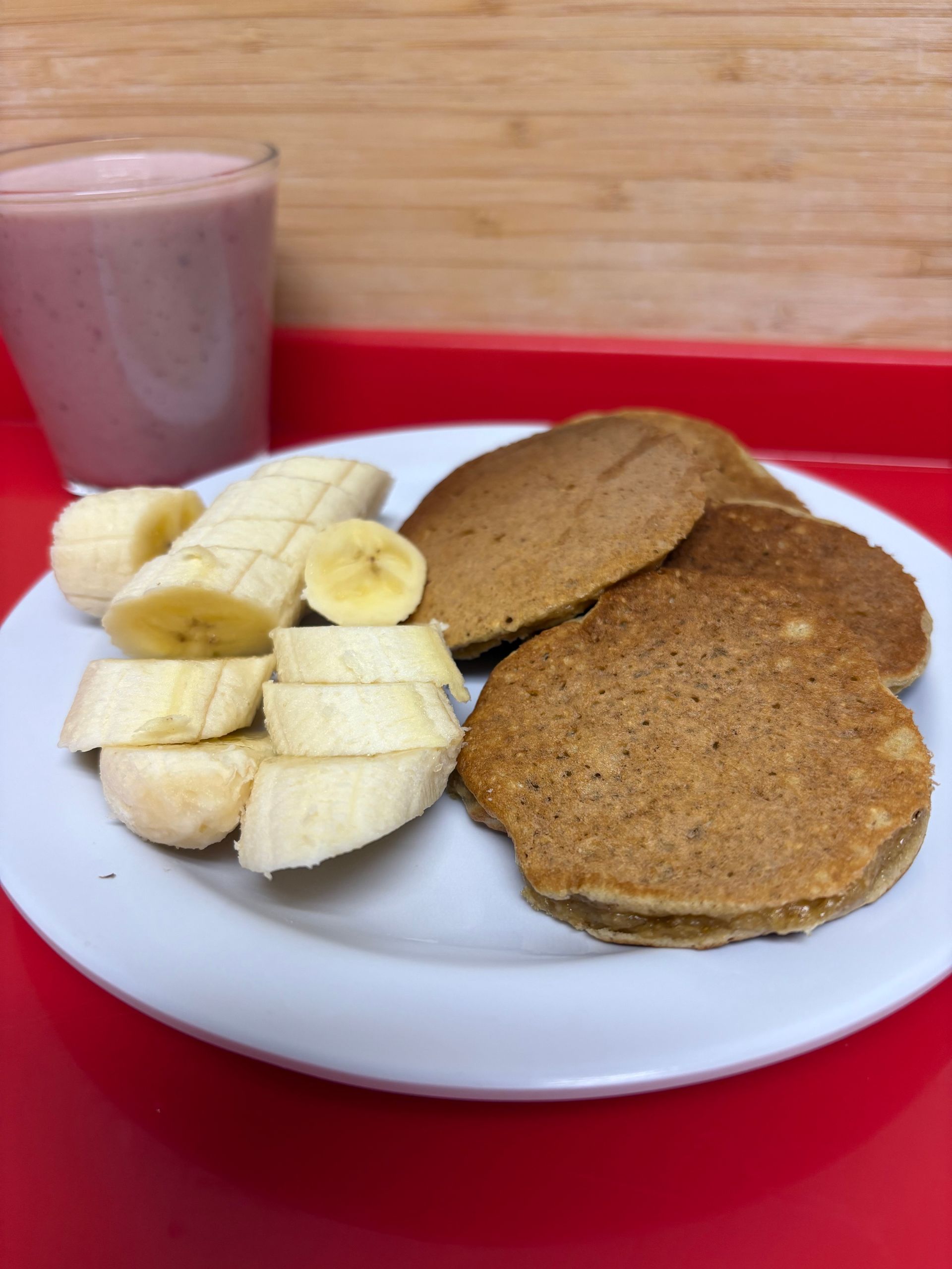 A white plate topped with pancakes and bananas next to a smoothie