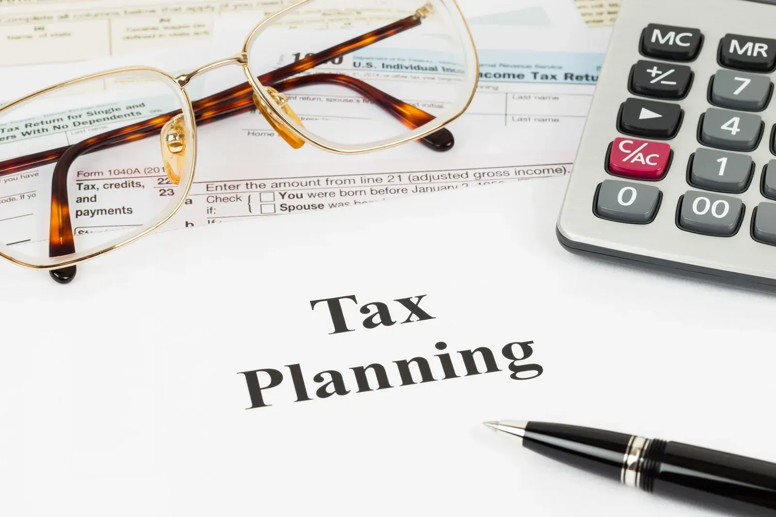 A calculator , alarm clock , pen , notebook and sticky note with the word tax on it.