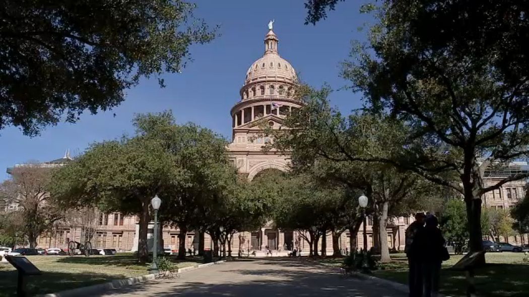Texas State Capitol building framed by trees and a pathway on a sunny day.