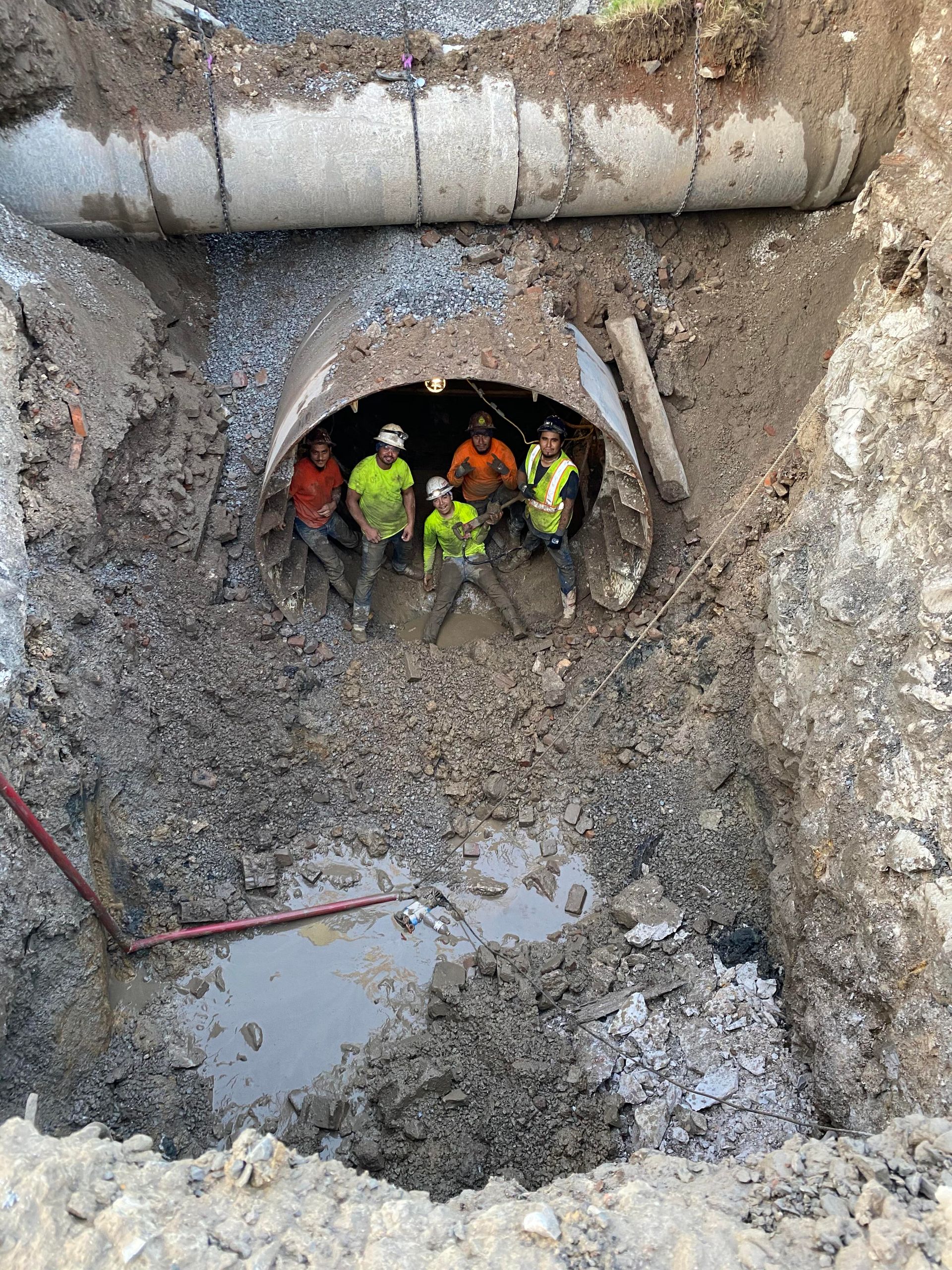 Construction workers inside a dug-out pipe. They are wearing bright vests and looking at the camera.