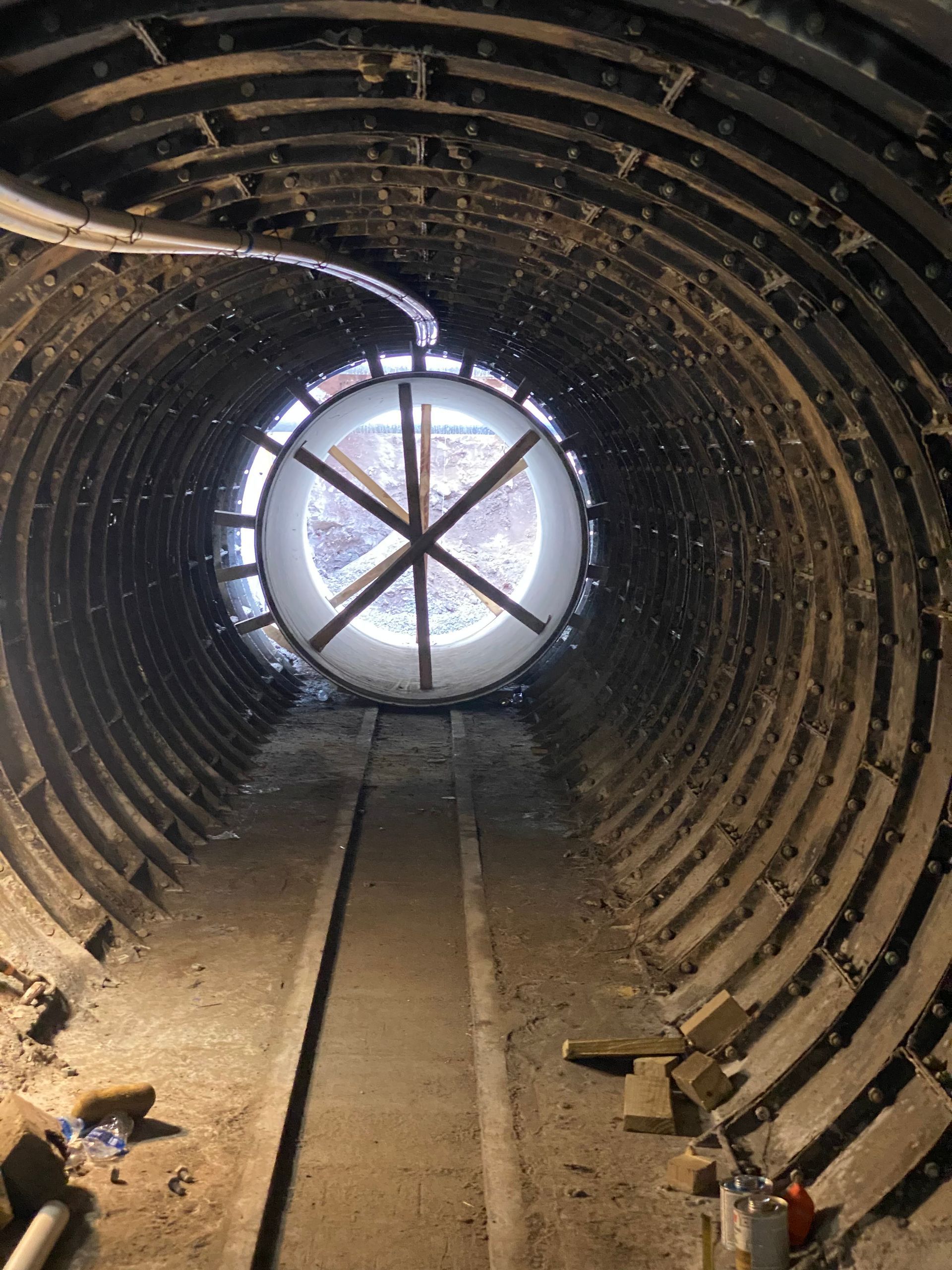 Inside of a cylindrical tunnel, looking towards a circular window with support beams.
