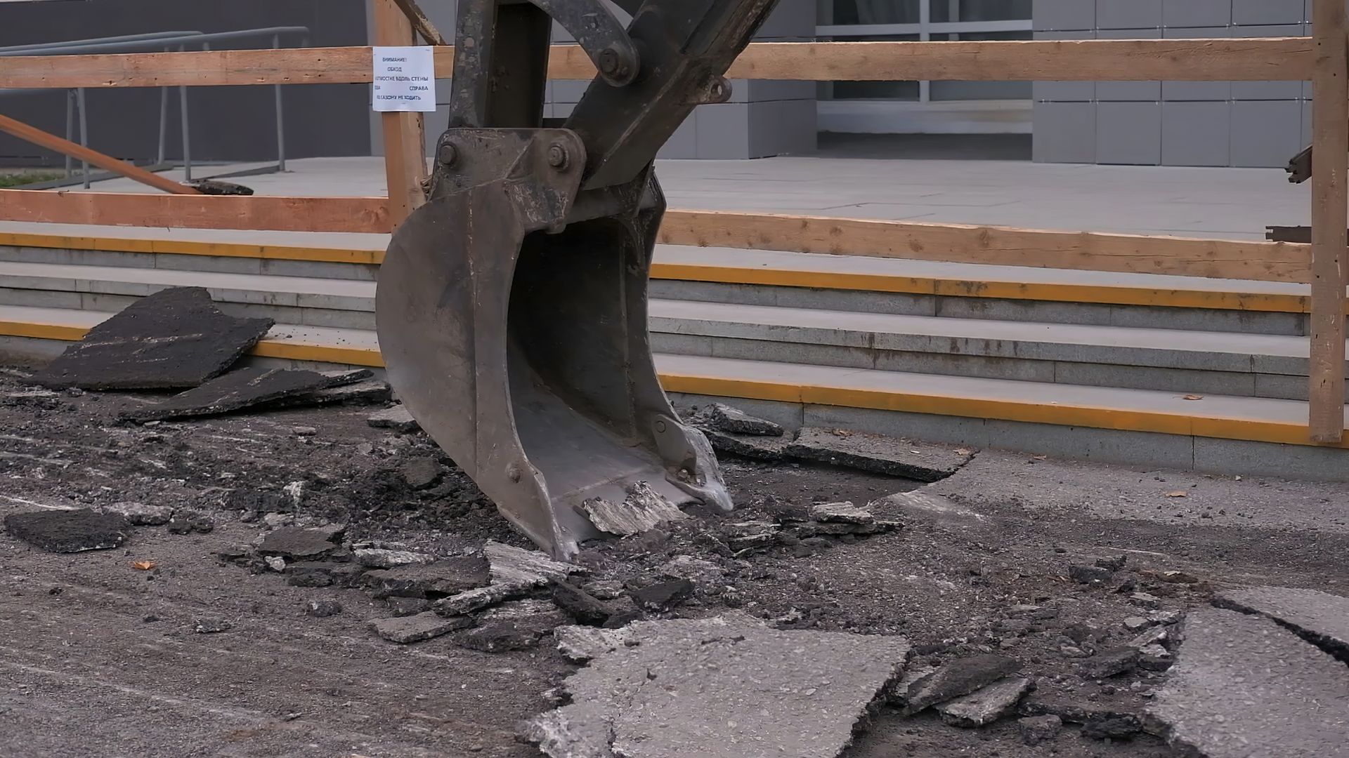 An excavator bucket breaking up asphalt on a construction site.
