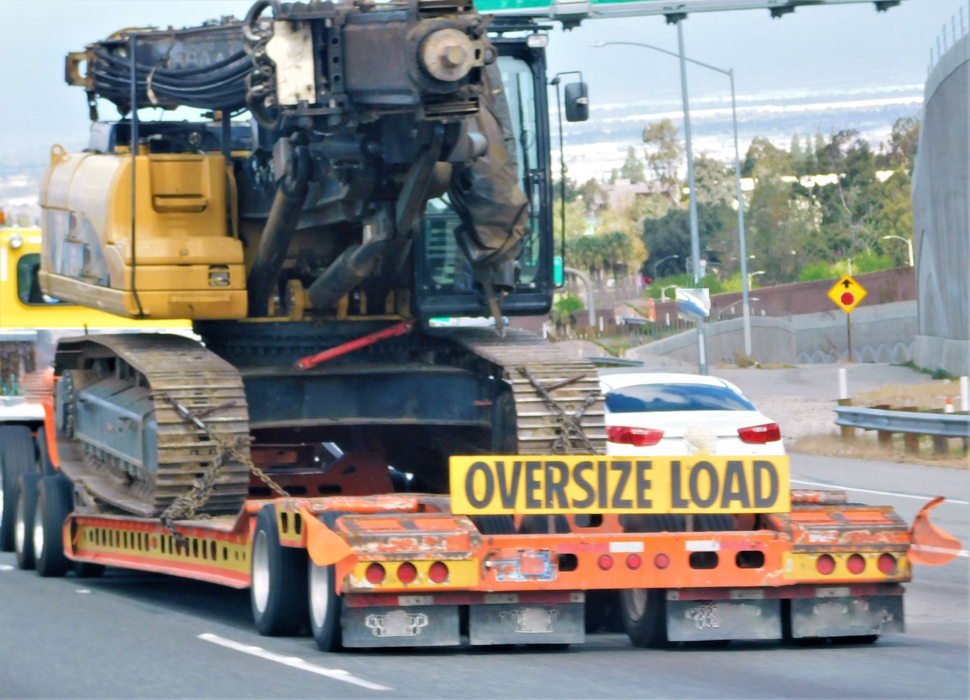 Oversized yellow construction equipment on a lowboy trailer, labeled