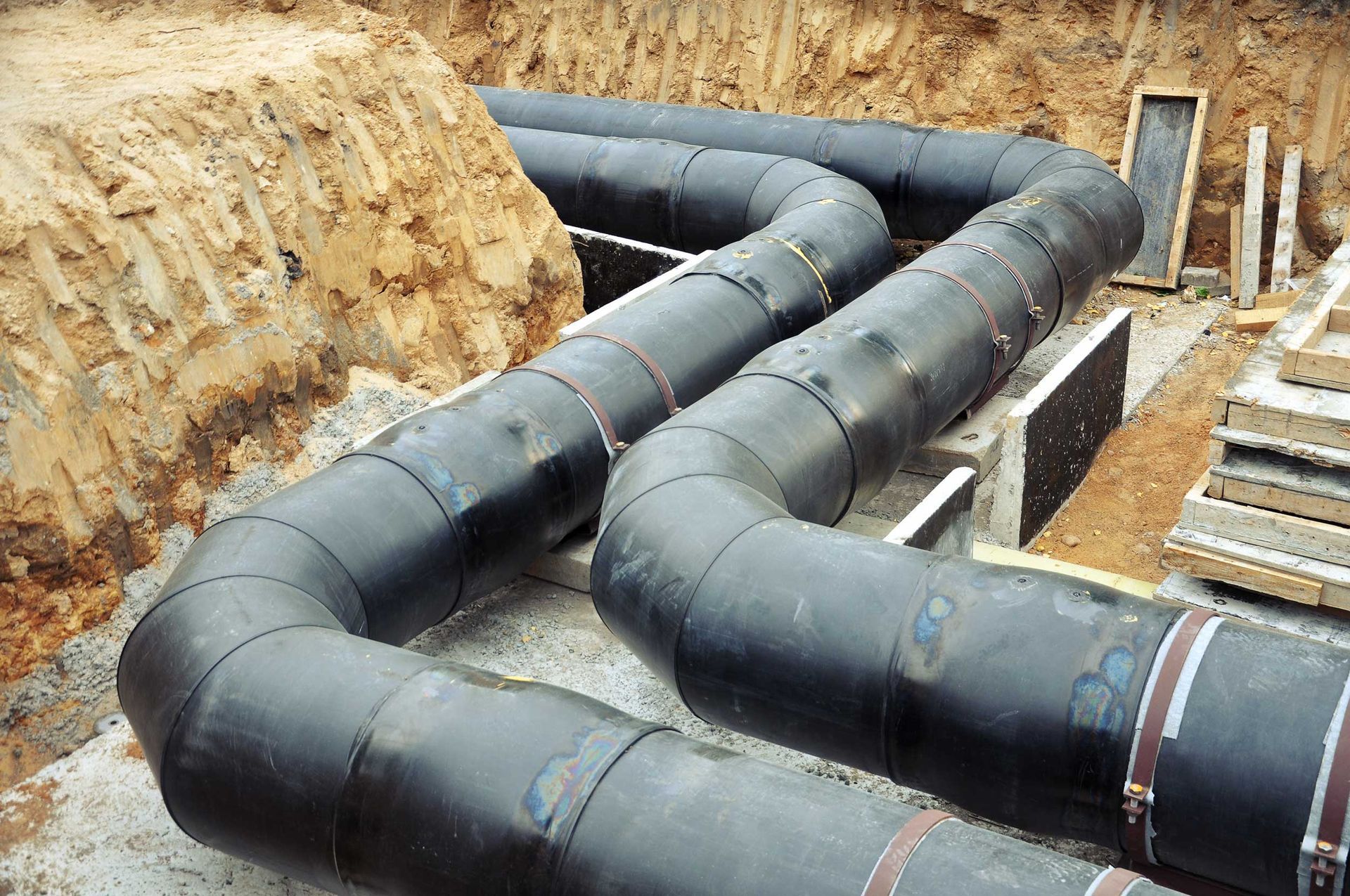 Black pipes snaking through a trench, possibly for a utility project. Earth tones surround.