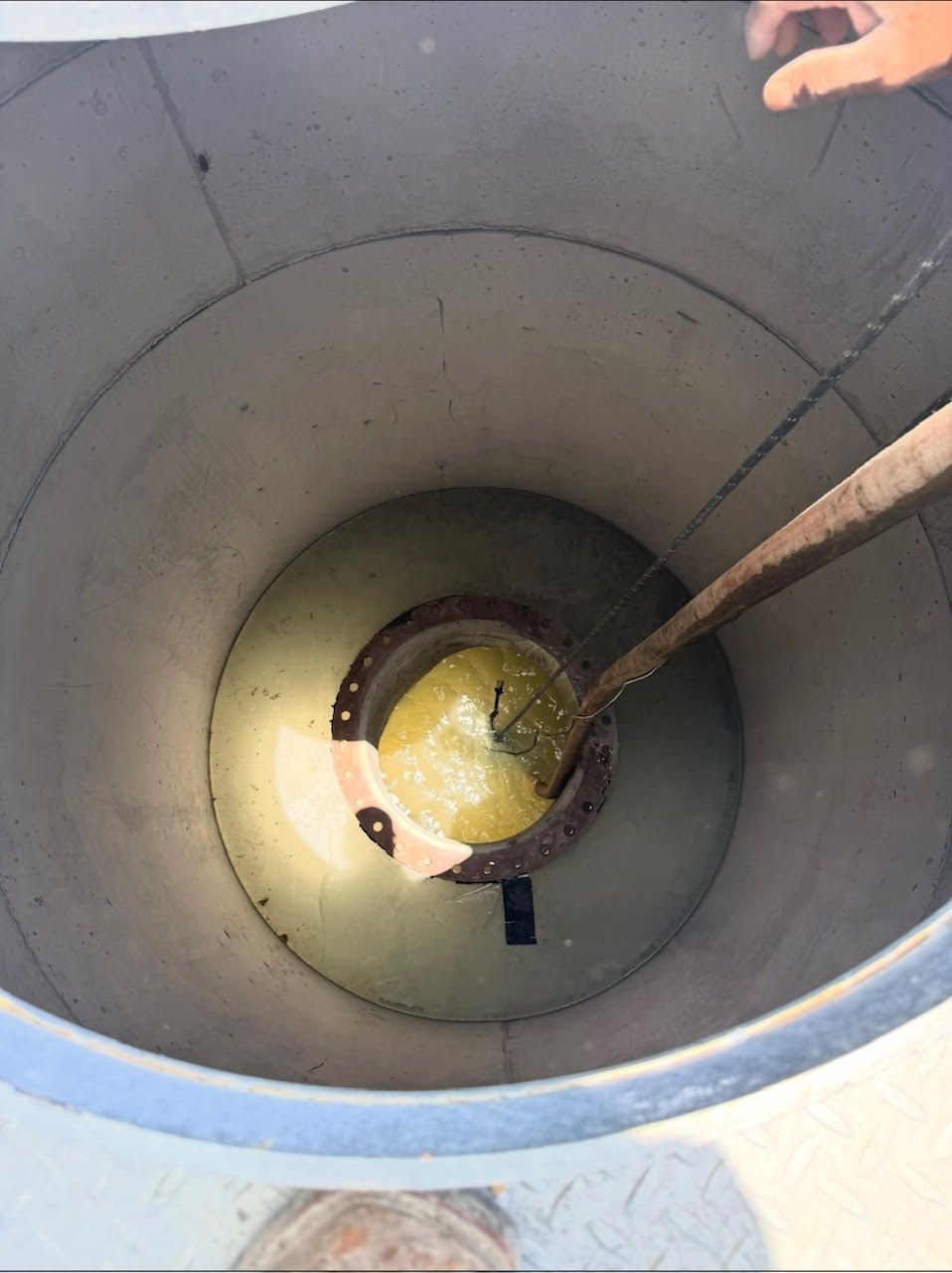 Looking down into a cylindrical tank with a yellow liquid at the bottom and a tool suspended inside.