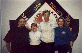 Four people posing in front of a martial arts academy logo.