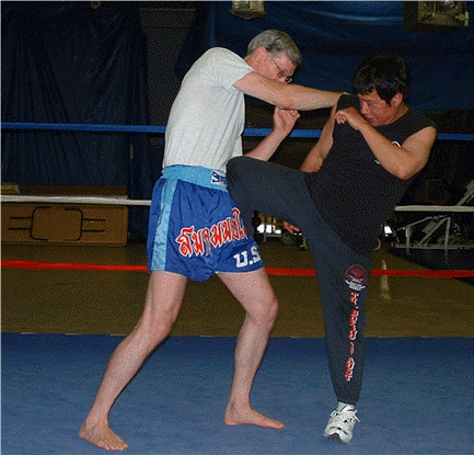 Man in blue shorts blocks kick from another man in a boxing ring.